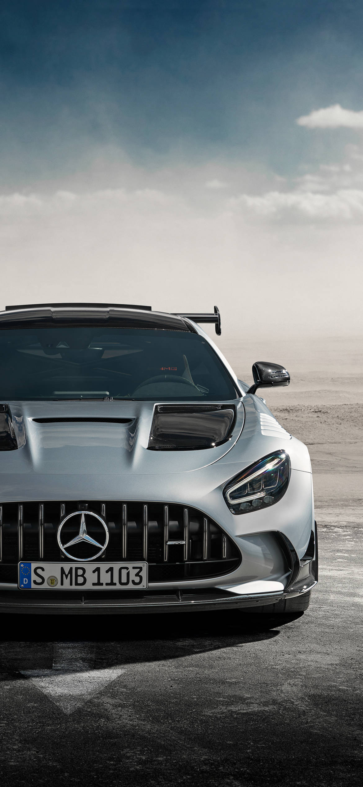 銀色梅賽德斯-AMG iPhone 壁紙 — 一架銀色 Mercedes-AMG GT R 賽車在陰天嘅塵土賽道上蓄勢待發。