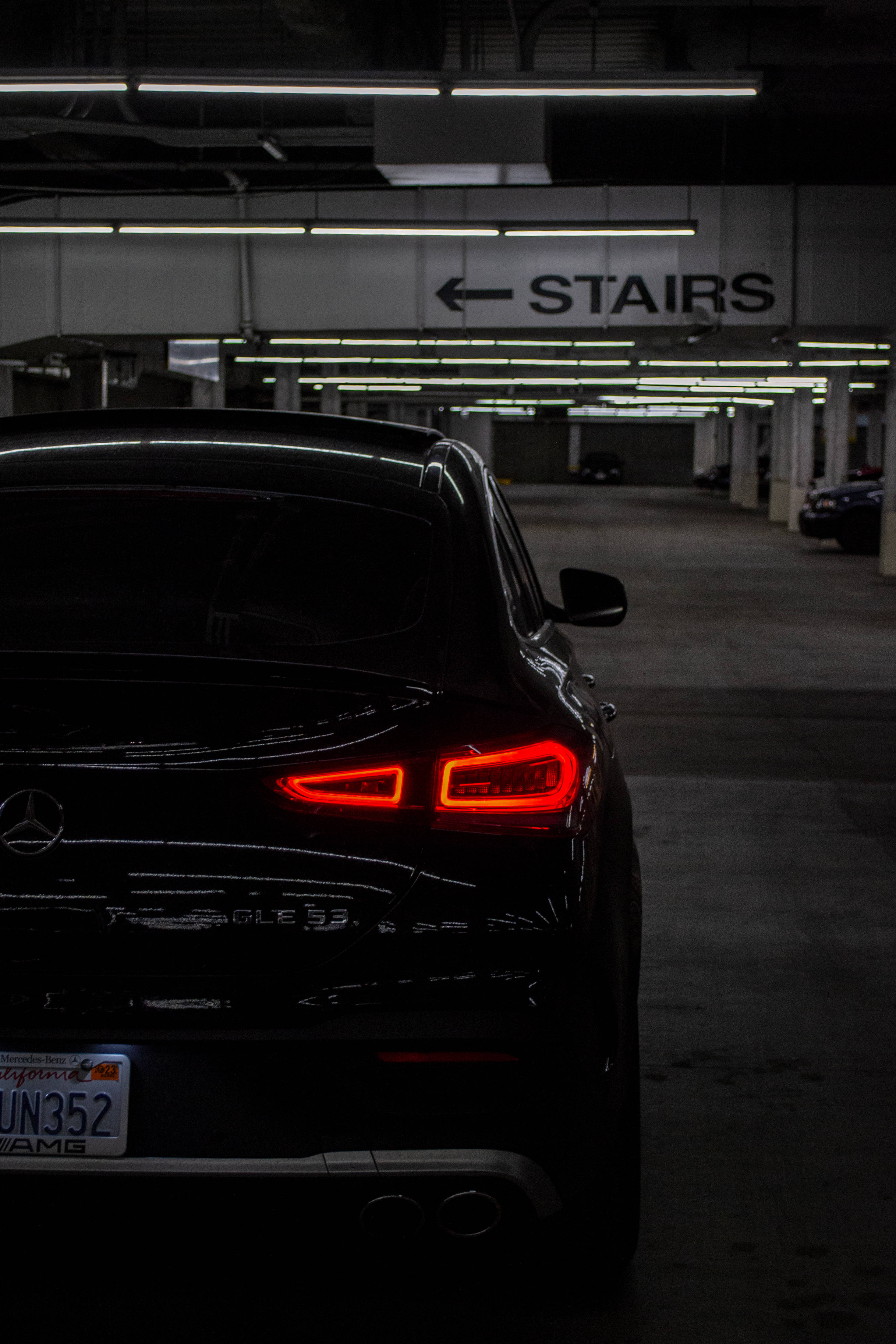AMG 紅色尾燈 iPhone 壁紙 — 一輛黑色Mercedes-AMG GLC 63 SUV的發光紅色尾燈在光線昏暗的地下停車場中格外醒目。