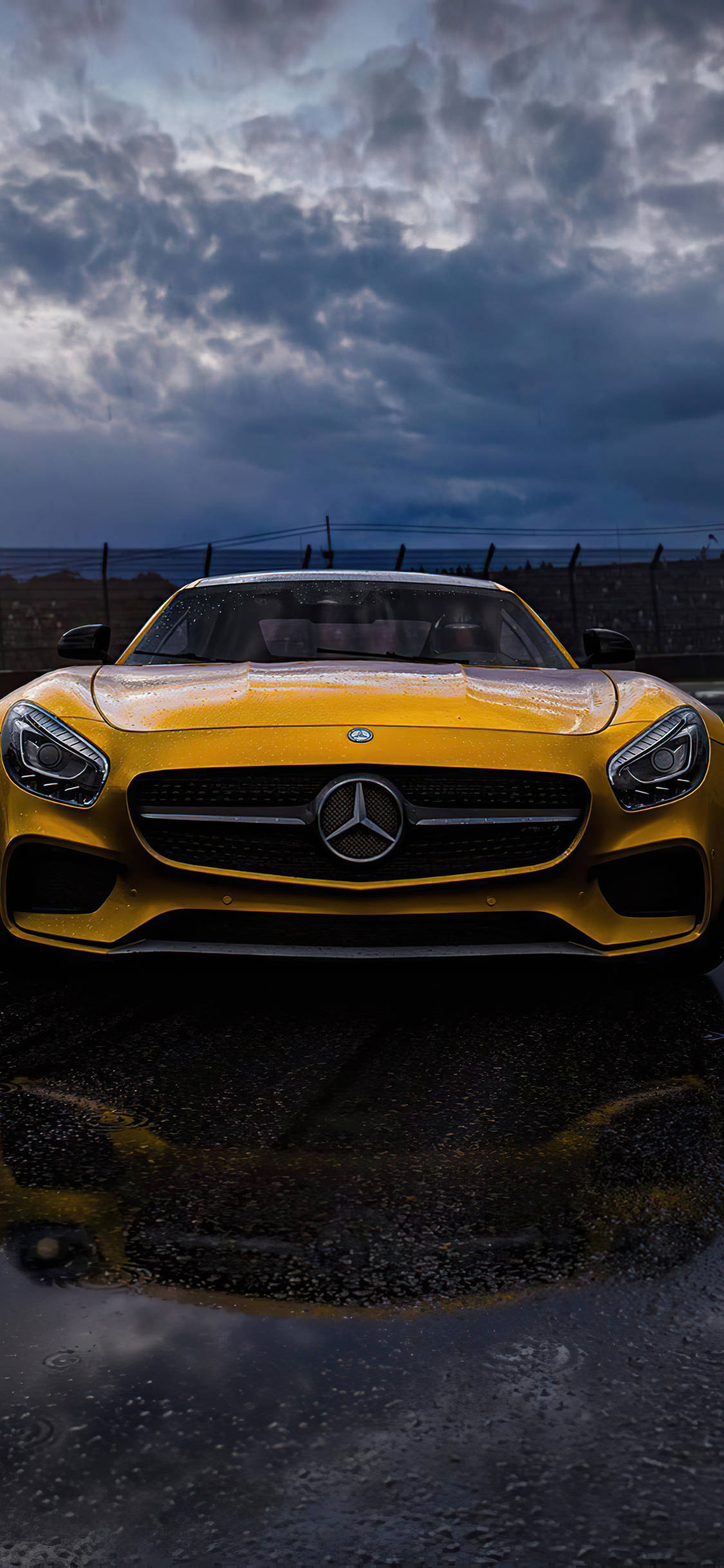 梅賽德斯-AMG iPhone 壁紙 — 一輛鮮黃色的 Mercedes-AMG GT 跑車在戲劇性的暴風雨天空下閃閃發光，倒映在濕漉漉的瀝青路面上。