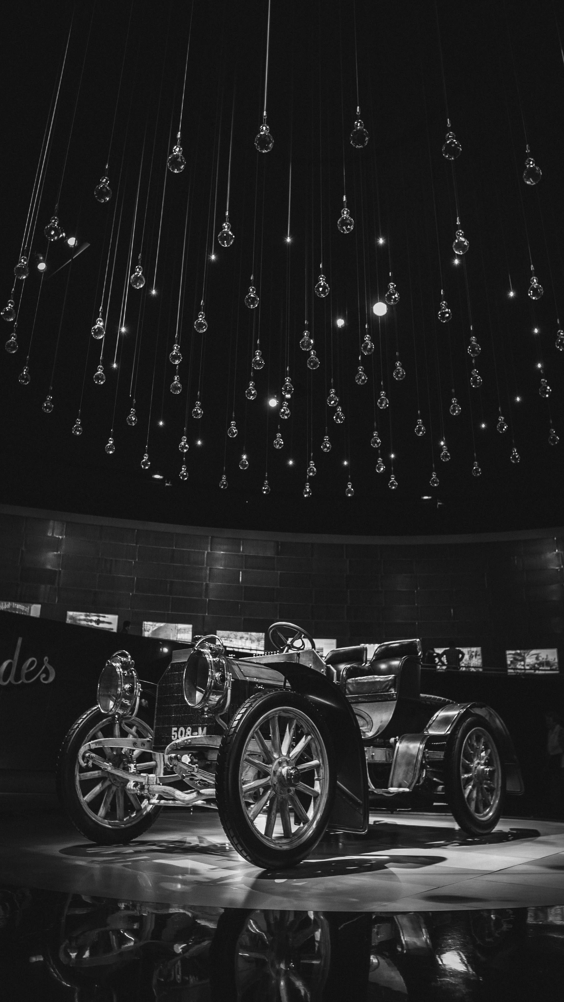 梅賽德斯-AMG SL 300 壁紙 — 一輛復古汽車在單色博物館展覽中，在懸掛的玻璃燈泡下閃閃發光，地板具有反射效果。