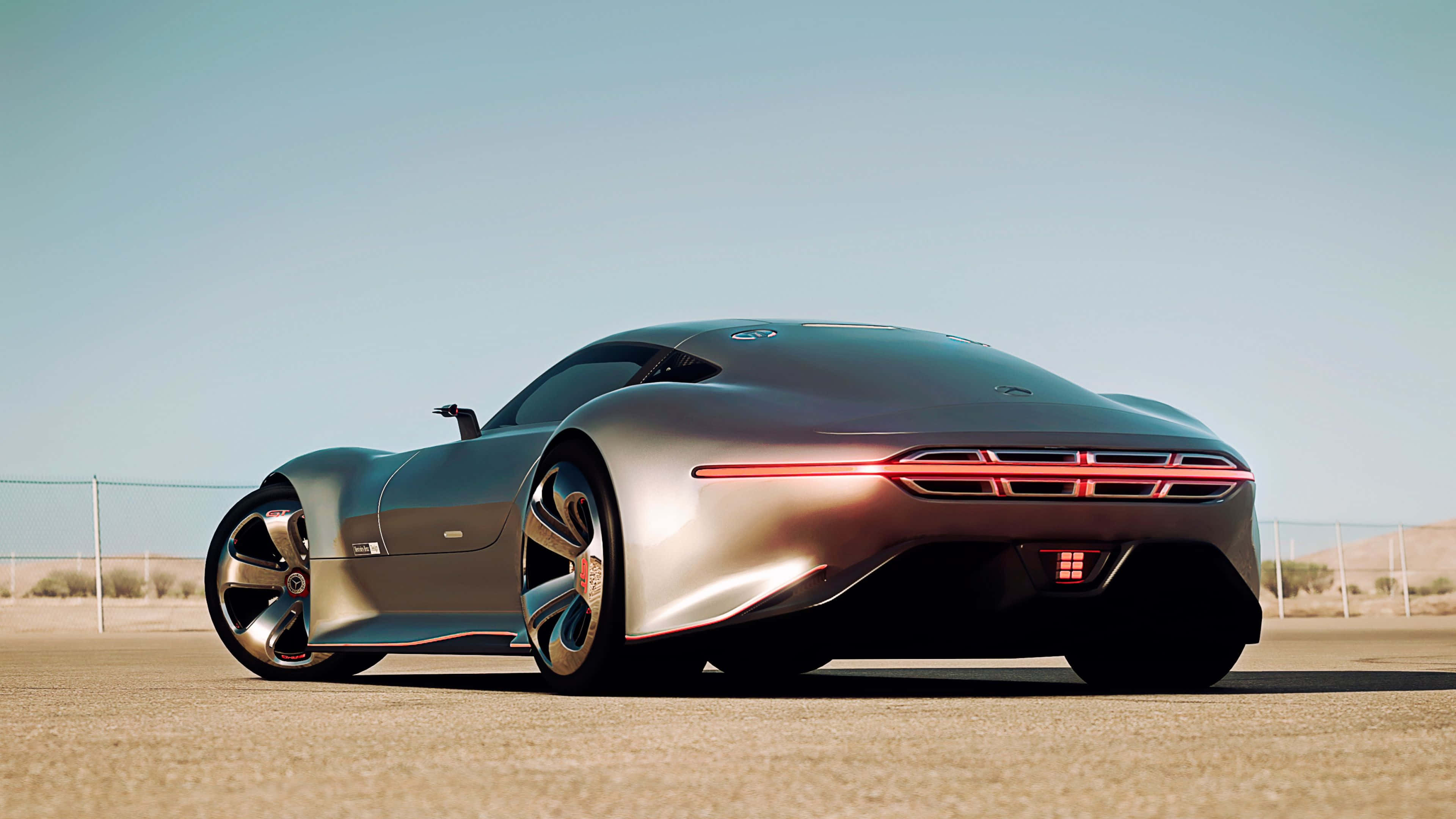 梅賽德斯-奔馳AMG Vision Gran Turismo 壁紙 — 一輛時尚的銀色未來主義跑車，帶有發光的紅色尾燈，停在沙漠公路上，天空清澈湛藍。