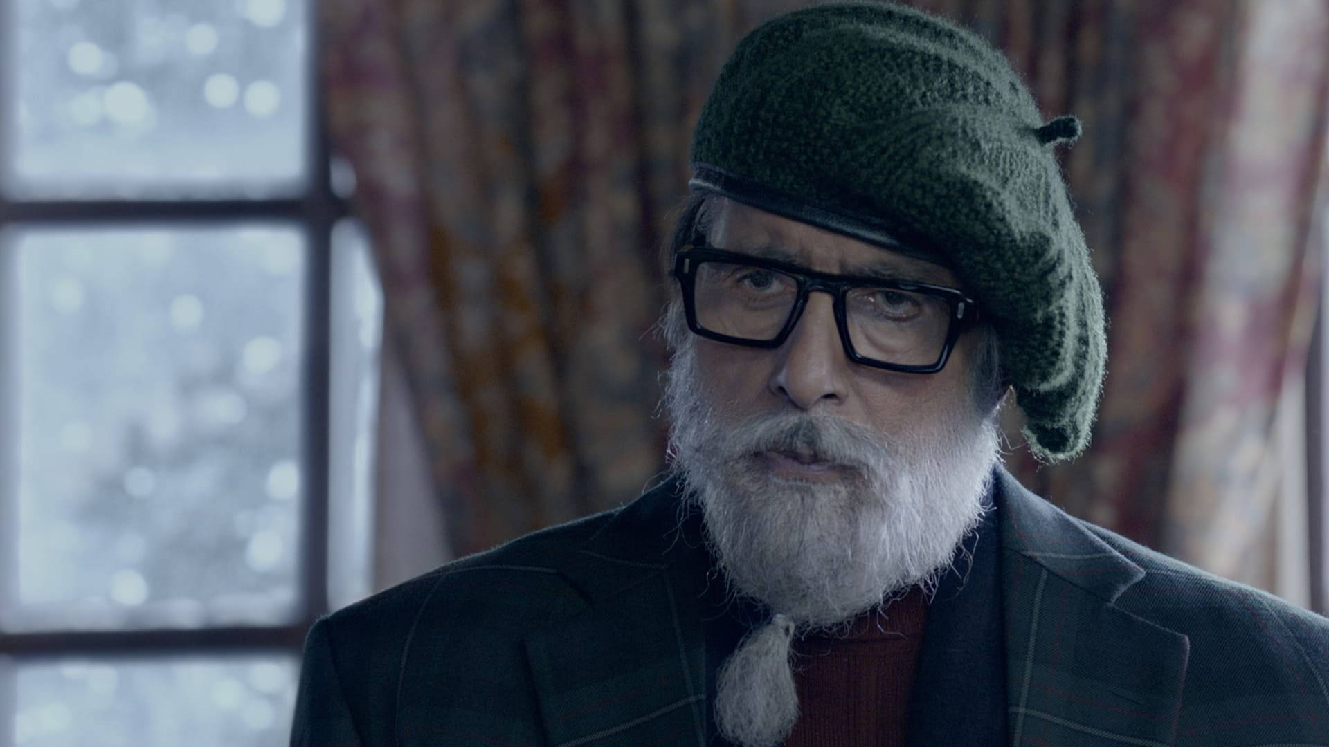 偉大演員 Amitabh Bachchan 壁紙 — 一位留著白鬍子、戴著綠色針織帽的老人，透過窗戶凝視著外面可見的雪花。