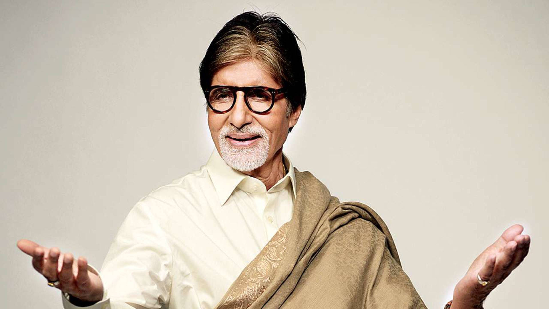 美學 Amitabh Bachchan 壁紙 — 一位戴眼鏡、披米色披肩的長者，在純色背景前敞開手勢。