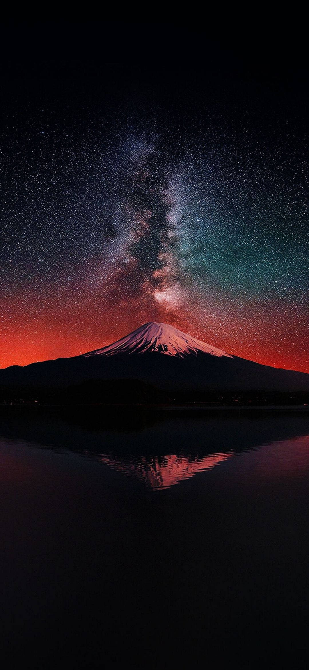 AMOLED 雪山 壁紙 — 白雪覆蓋的富士山在充滿活力的星空下形成剪影，銀河拱橋般橫跨天際，倒映在下方平靜的水面上。