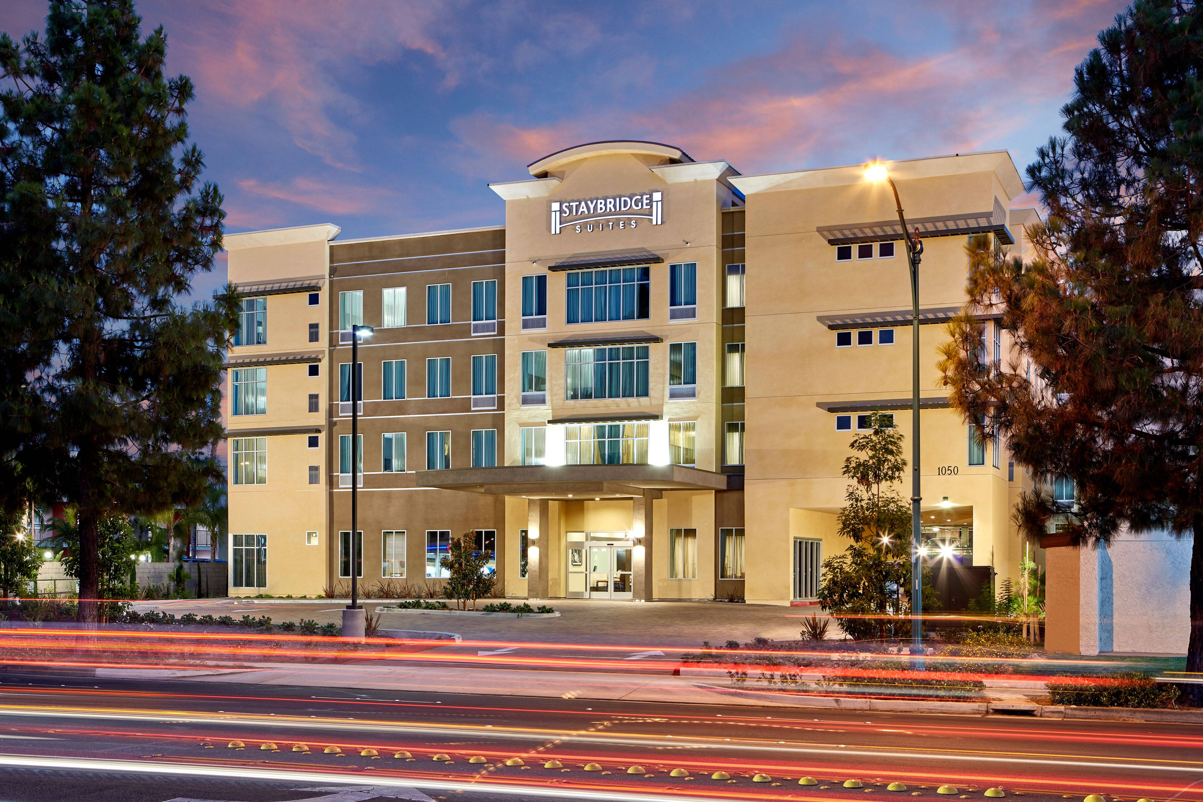 於 Anaheim Staybridge Suites 享受舒適住宿 壁紙 — 一座現代酒店建築在黃昏時亮起燈光，繁忙街道上汽車燈光飛馳而過形成光軌。