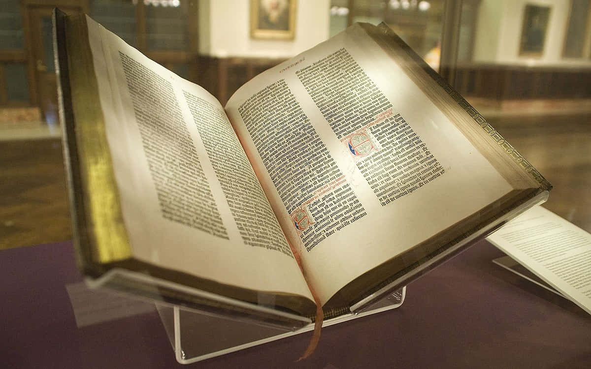  壁紙 — 一本古老的彩繪手稿書，打開展示在玻璃陳列櫃中，帶有金色邊緣和紅色墨水首字母。