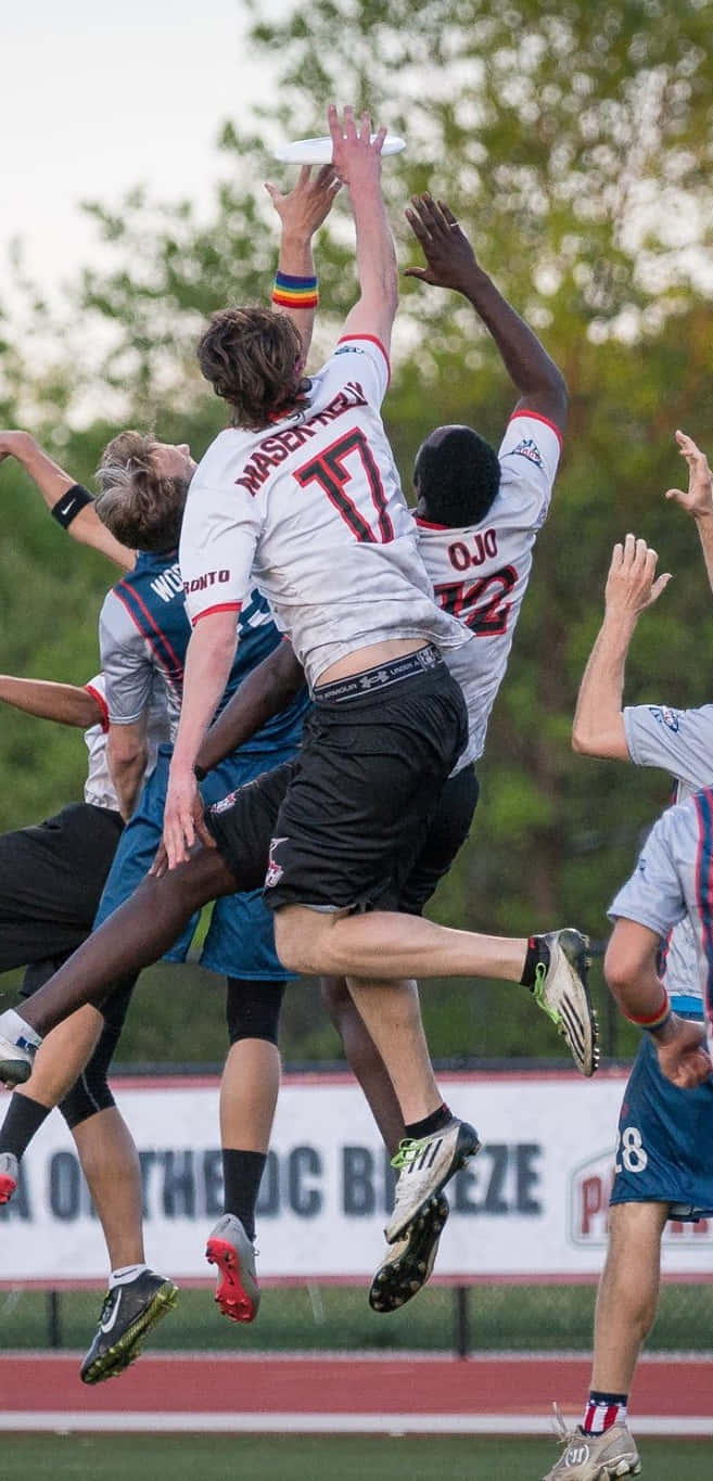 Android Ultimate Frisbee 背景：男運動員跳躍爭奪飛盤 壁紙 — 球員在草地上進行激烈的終極飛盤比賽時，高高躍起爭奪飛行的飛盤。