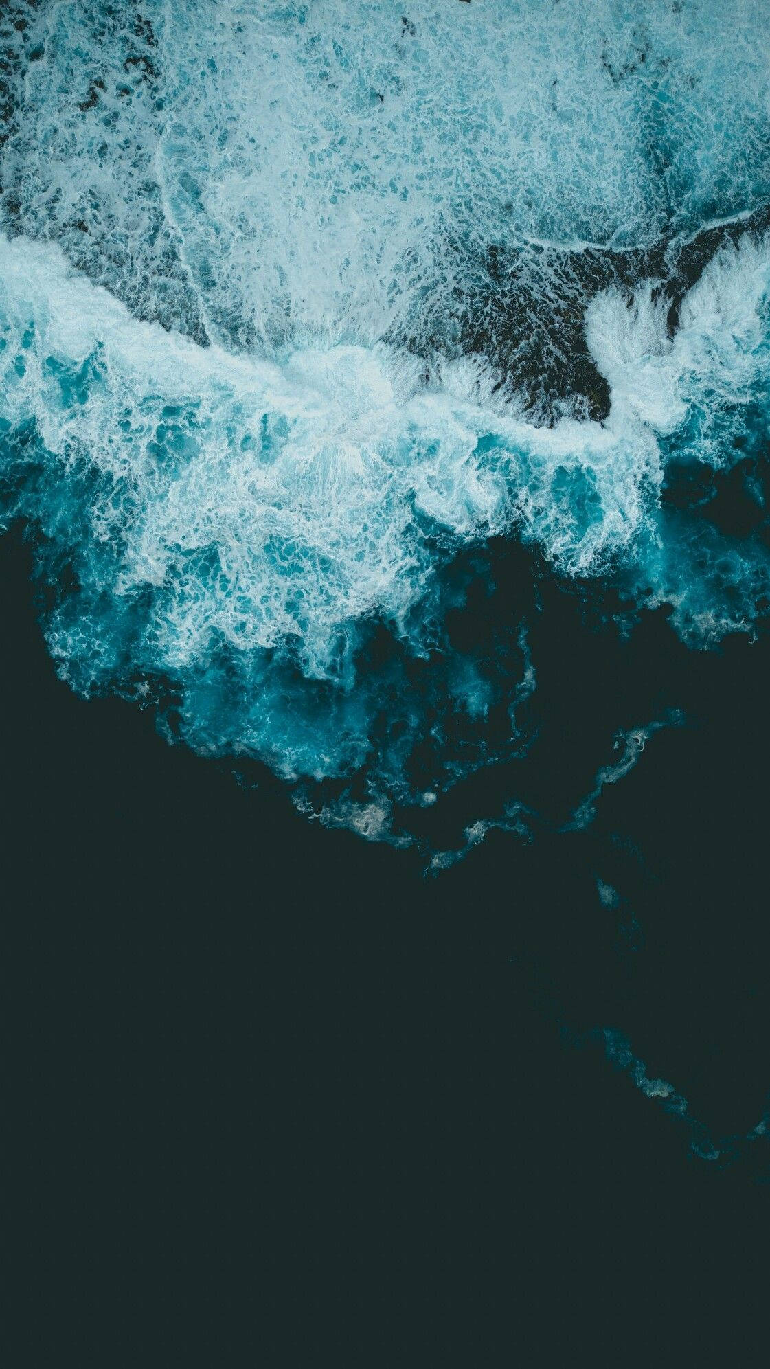 深色海洋波浪酷Android壁紙 壁紙 — 從高空俯瞰，碧綠色的海浪拍打著黑暗的海岸，激起白色泡沫般的浪花。