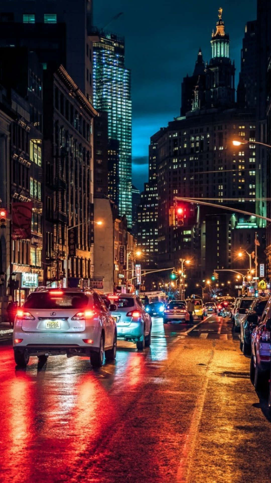 Android 紐約市的城市生活 壁紙 — 雨夜中濕滑的城市街道，在 towering 的燈火通明摩天大樓下，汽車尾燈在濕漉漉的路面上反射出光芒。