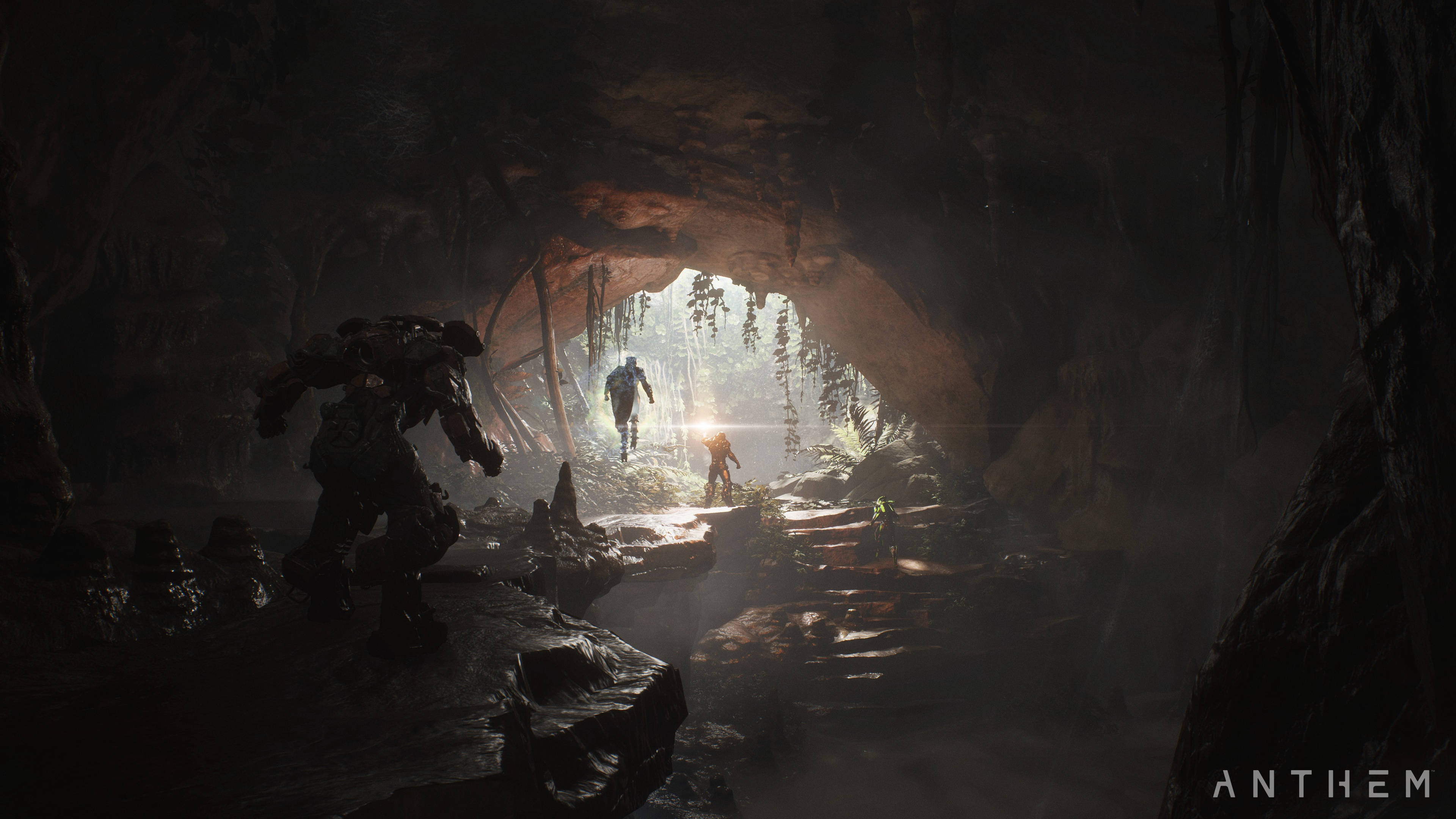 Anthem 4K 洞穴場景 壁紙 — 剪影般的裝甲人物從黑暗洞穴中出現，進入陽光明媚、有霧氣和懸掛藤蔓的叢林空地。