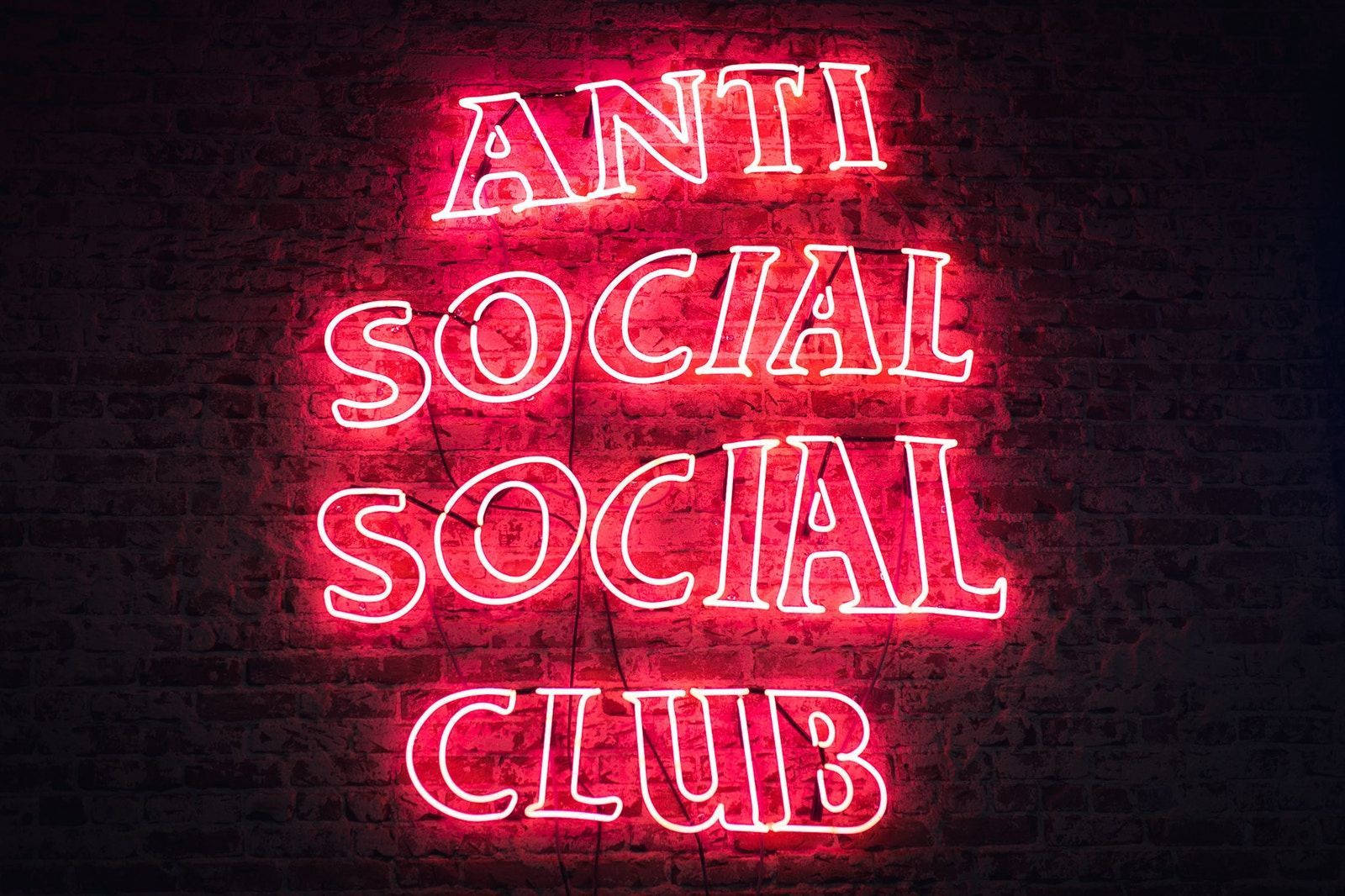 Anti Social Social Club 紅色霓虹 壁紙 — 一個發光的紅色霓虹燈牌，上面寫著「ANTI SOCIAL SOCIAL CLUB」，以鮮豔的光芒照亮了深色的磚牆。