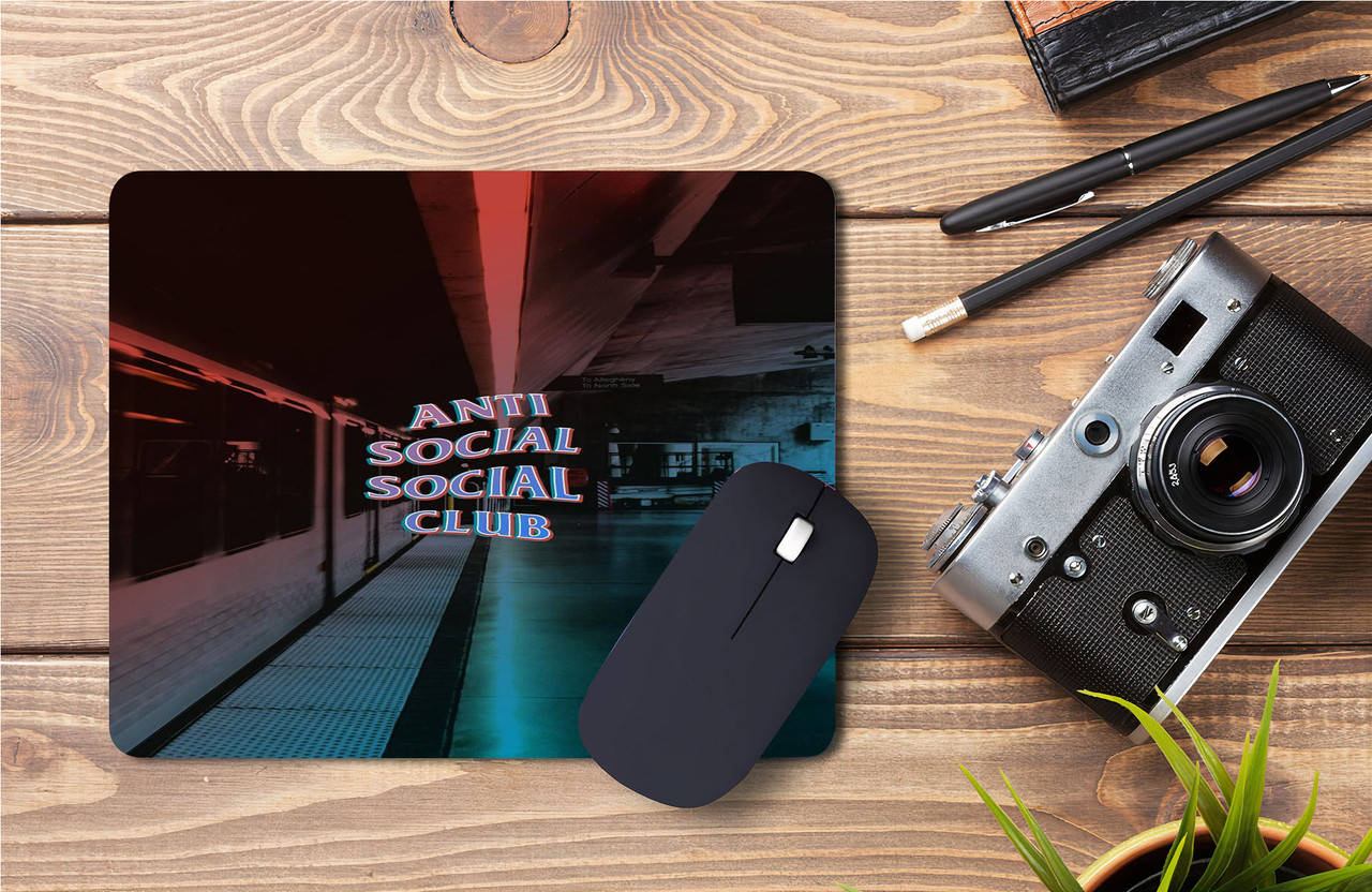 Anti Social Social Club滑鼠墊 壁紙 — 一個帶有 'Anti Social Social Club' 霓虹燈牌的地鐵站台滑鼠墊，放在木桌上，旁邊有一台復古相機和筆。