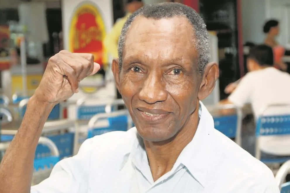 拳壇傳奇 Antonio Cervantes：賽場上的活傳奇 壁紙 — 一位灰白頭髮的長者在明亮的室內環境中微笑著舉起拳頭。
