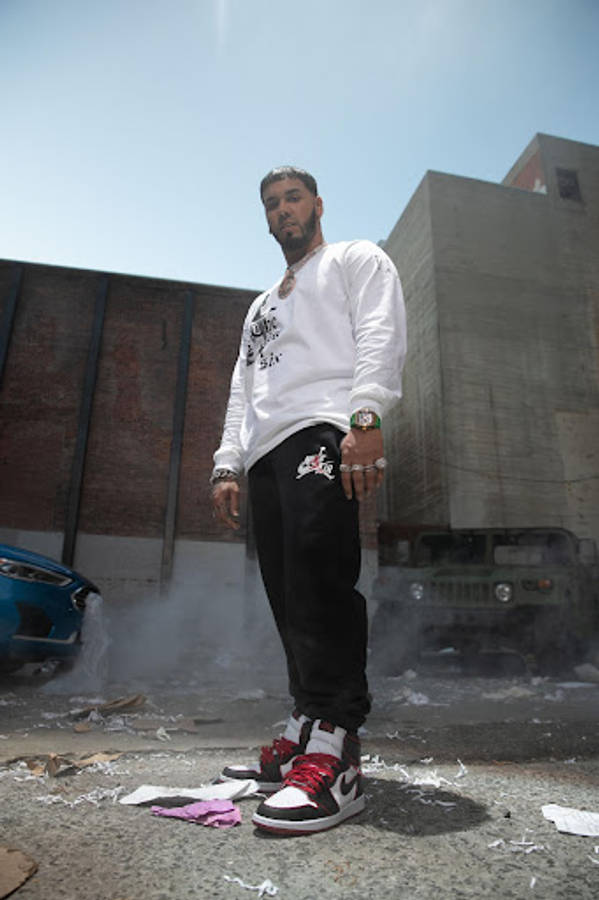 Anuel AA - 波多黎各超級巨星 壁紙 — 一名身穿白色長袖衫和黑色褲的男子自信地站在城市小巷中，煙霧在他腳邊升起。