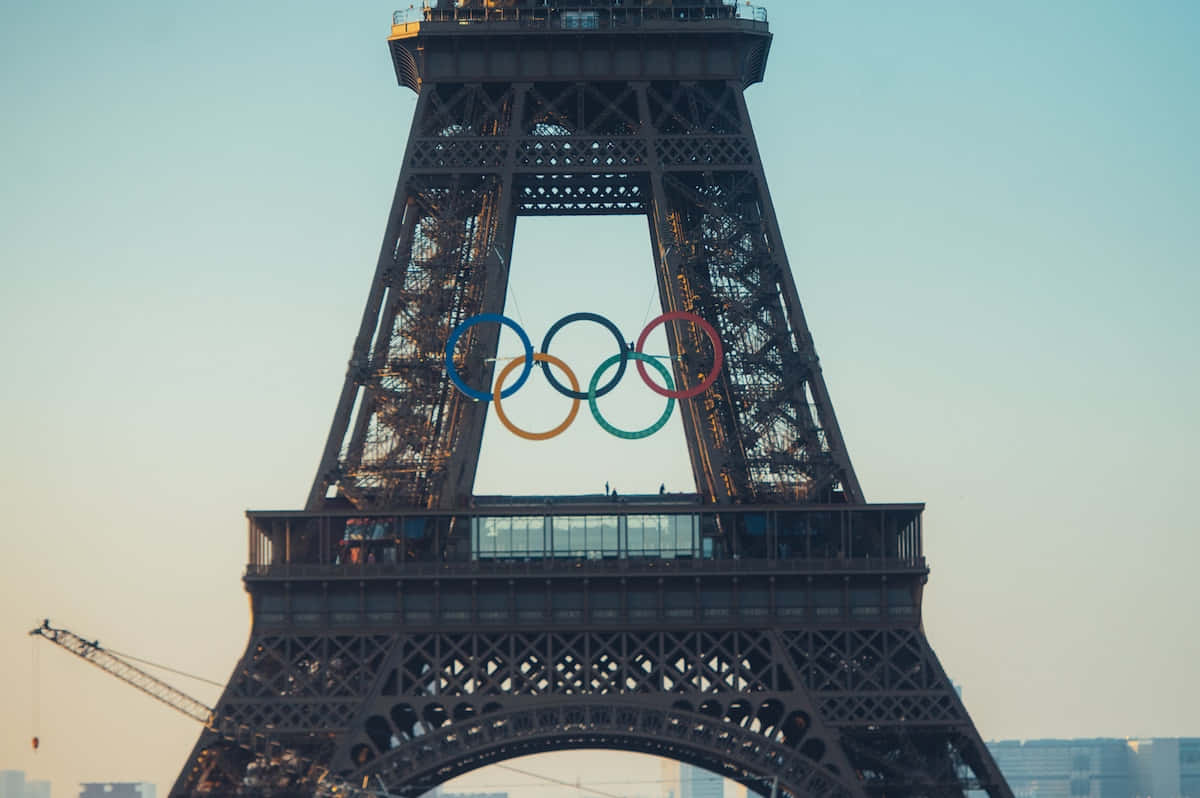  壁紙 — 奧運五環在黃金時刻醒目地懸掛在艾菲爾鐵塔的鐵格架上。