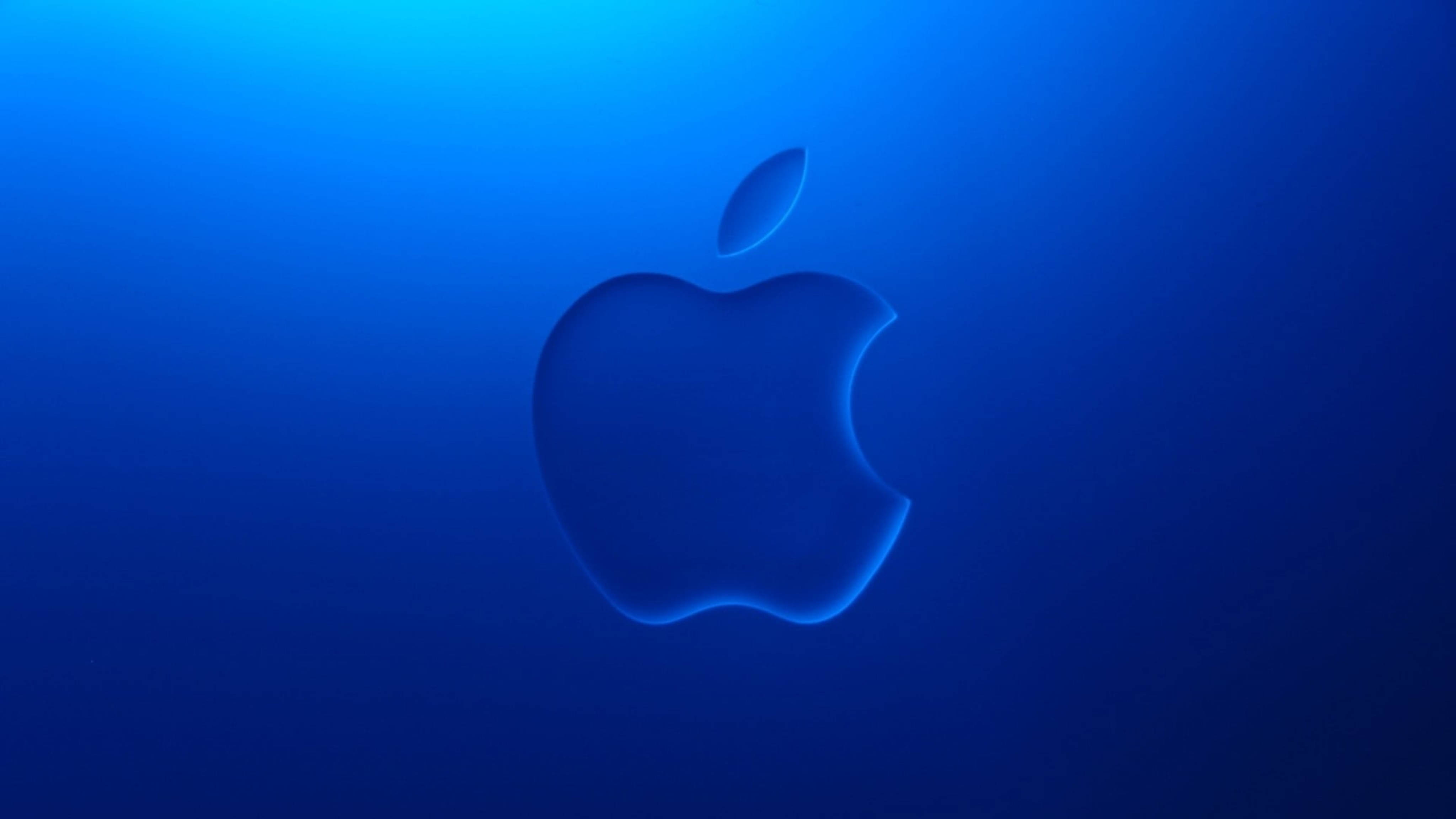 Apple 4K 超高清壓紋藍色背景 壁紙 — 一個發光的Apple標誌漂浮在漸變藍色背景上，柔和的光線從上方照射。