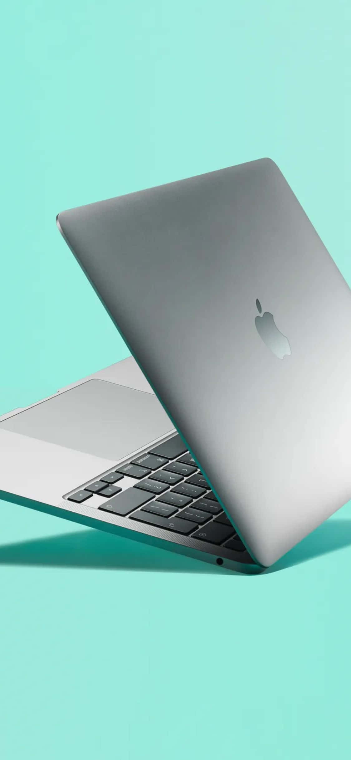 銀色 Apple 筆電薄荷綠背景 iPhone XS 壁紙 — 一部時尚的銀色 MacBook 手提電腦斜開在純薄荷綠色背景上。
