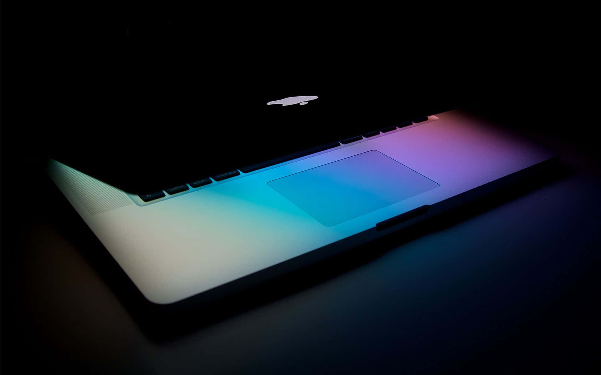 Apple MacBook Pro Retina 空間灰 壁紙 — 一部時尚的筆記型電腦在漆黑背景下散發出鮮豔的藍色和紫色背光。