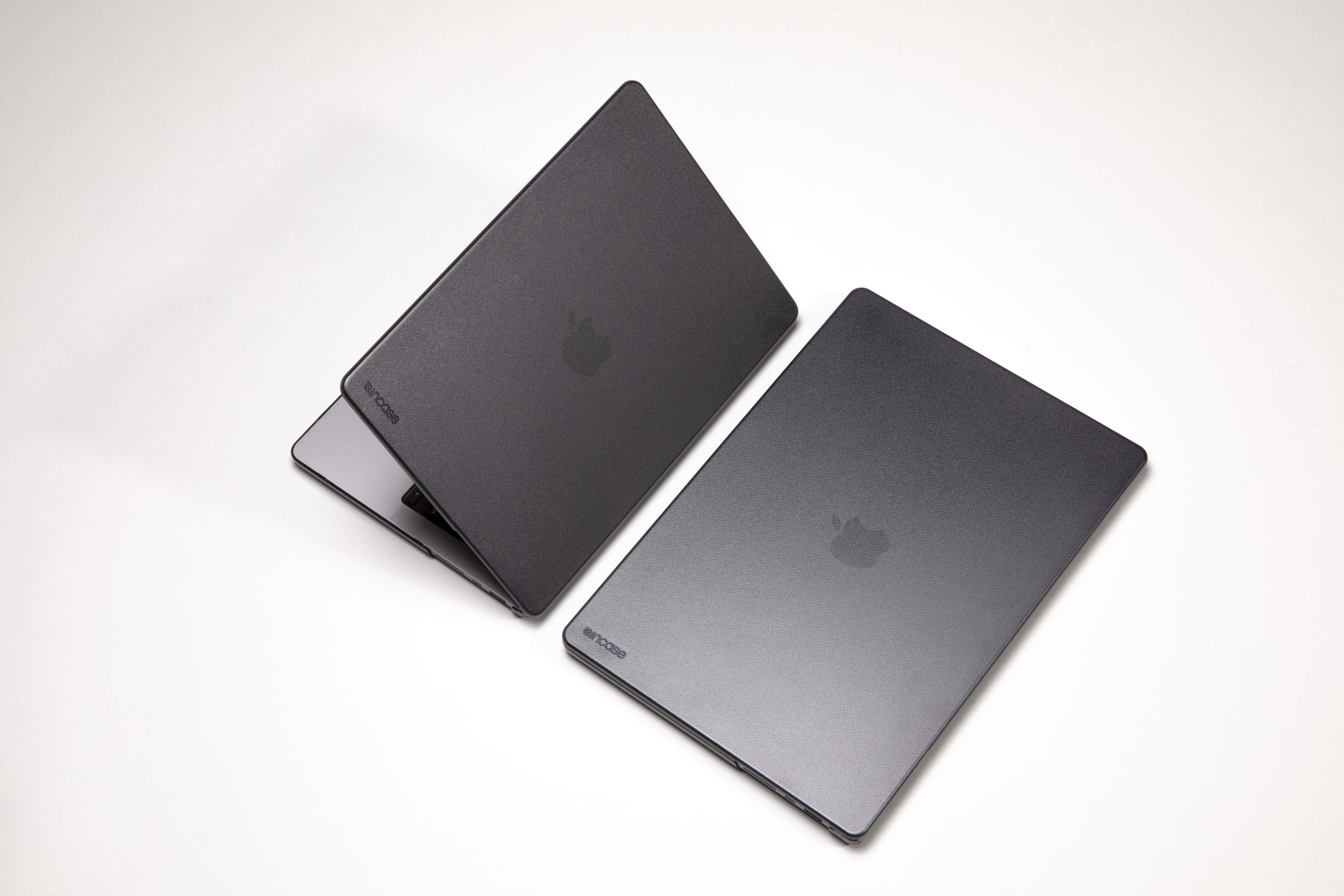 時尚黑色Apple MacBook 壁紙 — 兩部帶有Apple標誌的啞光黑色MacBook手提電腦，在柔和的影樓燈光下傾斜放置在潔白的表面上。