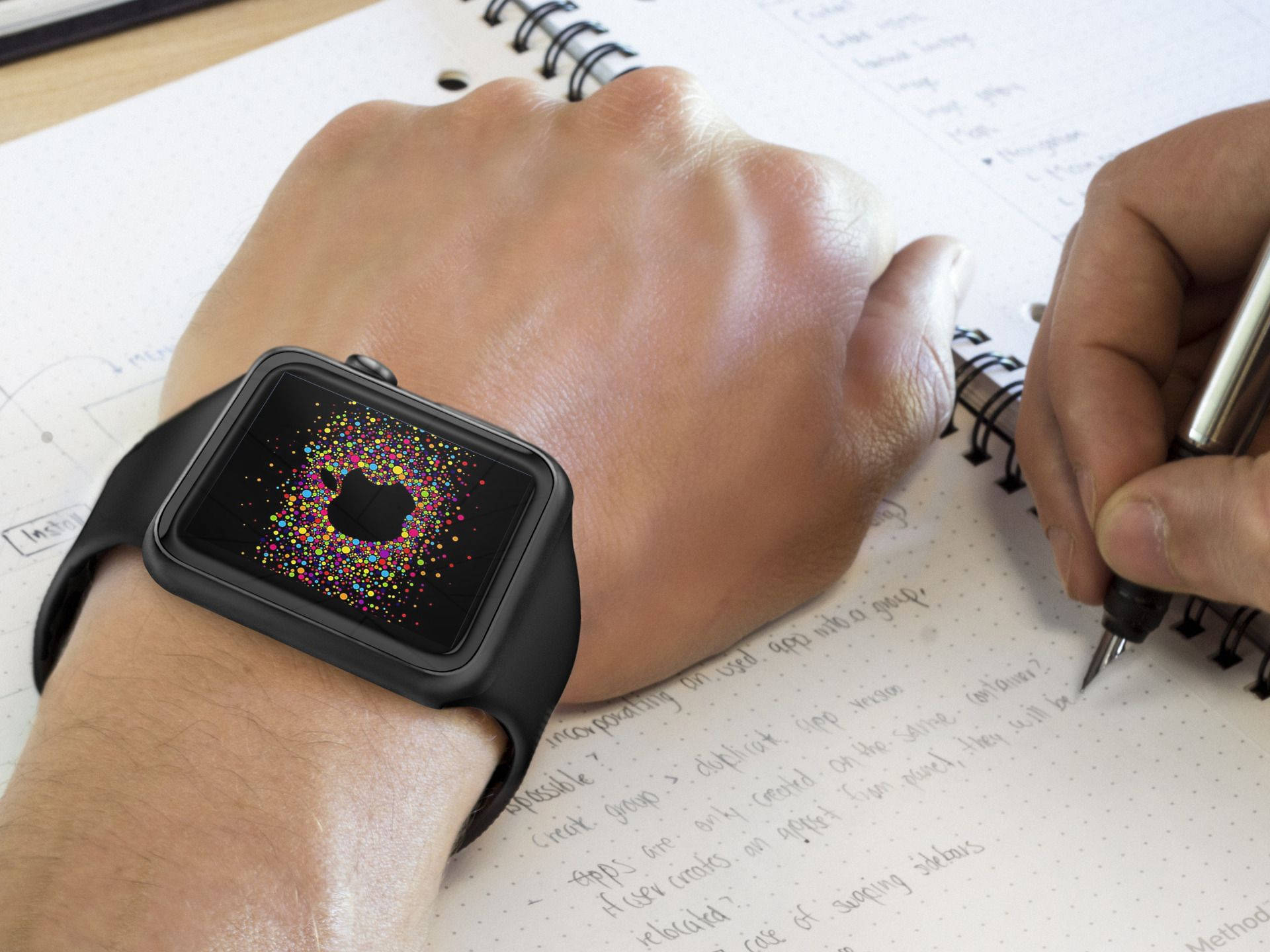 Apple Watch 黑色矽膠錶帶 壁紙 — 一隻手在螺旋筆記本上寫筆記，同時佩戴黑色Apple Watch，屏幕上顯示色彩繽紛的粒子動畫。