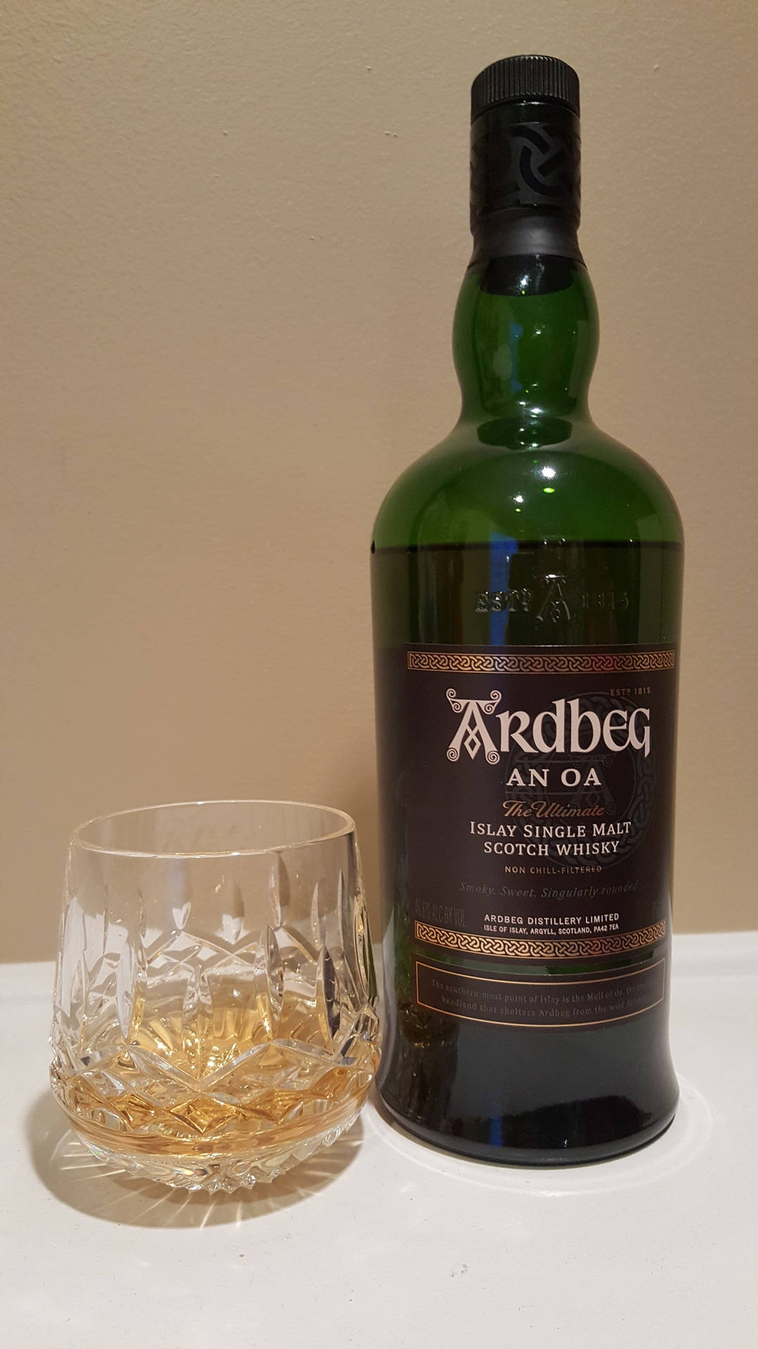 綠色威士忌酒瓶同裝滿琥珀色液體嘅水晶杯，喺白色表面上。