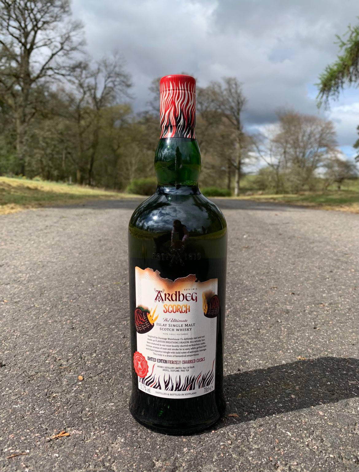 Ardbeg Scorch威士忌酒瓶置於道路上，有樹木和多雲天空。