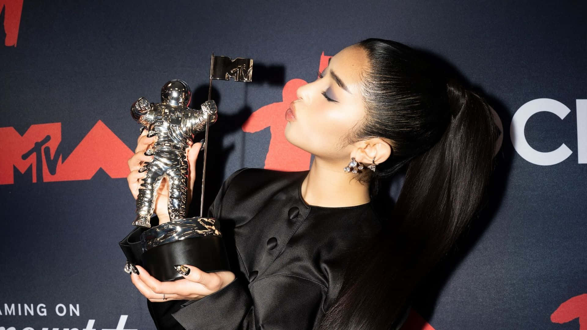  壁紙 — Ariana Grande 在帶有紅色標誌的深色背景下親吻她的MTV Moon Person獎項。