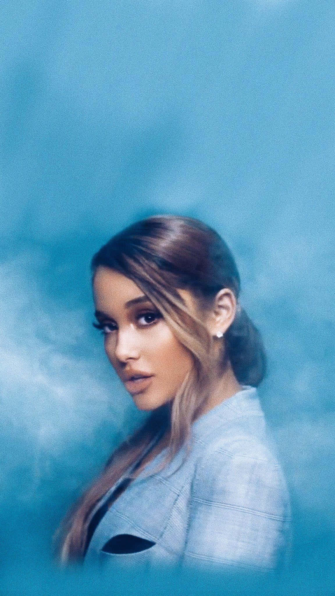 Aesthetic Ariana Grande 桌布 壁紙 — Ariana Grande 喺煙霧瀰漫嘅氛圍燈光下，溫柔咁凝視住模糊嘅藍色背景。