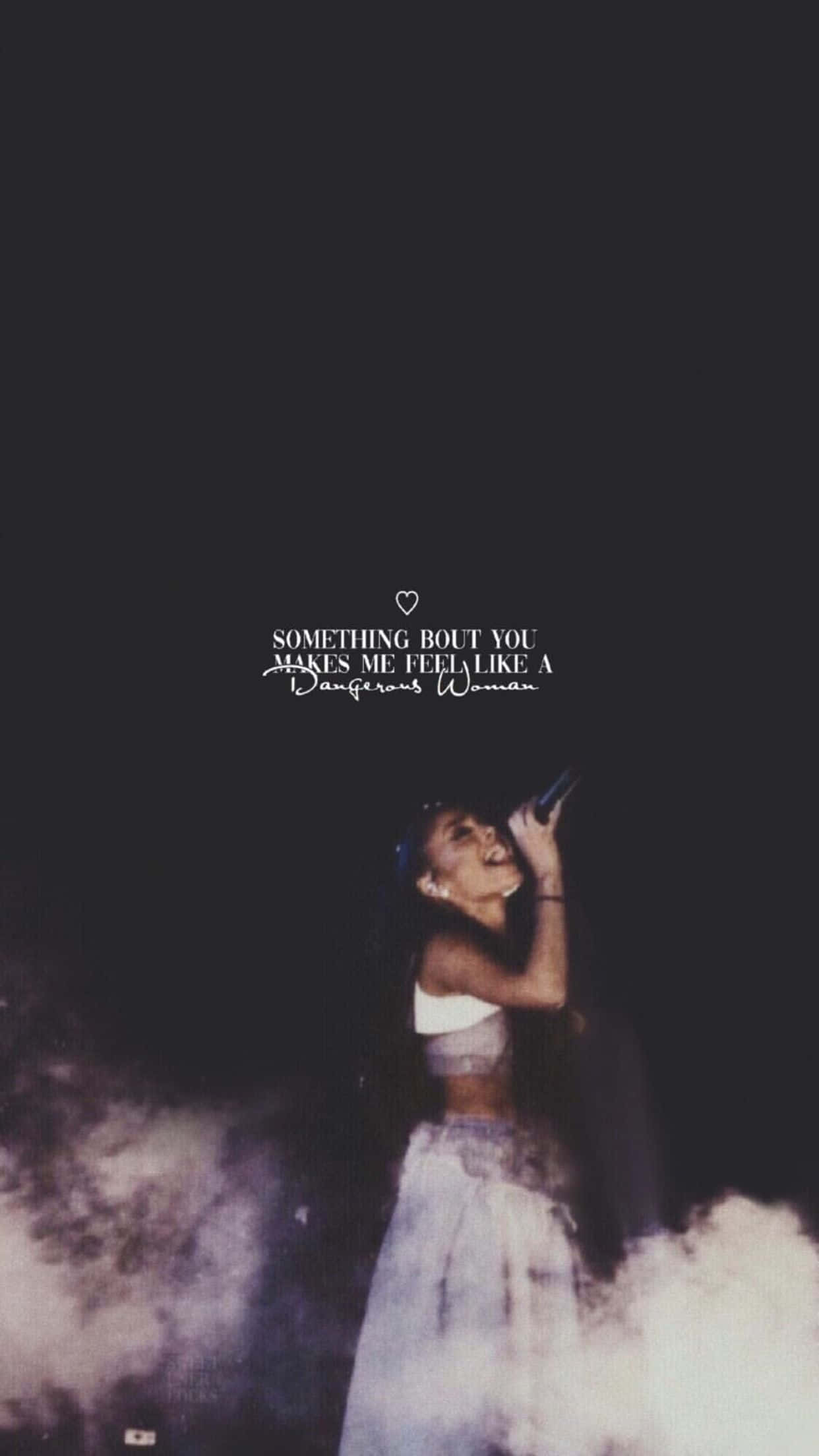 Aesthetic Ariana Grande 桌布 壁紙 — Ariana Grande 在夜晚煙霧彌漫的舞台上表演，燈光戲劇化，她上方有文字 'Something Bout You Makes Me Feel Like A Dangerous Woman'。