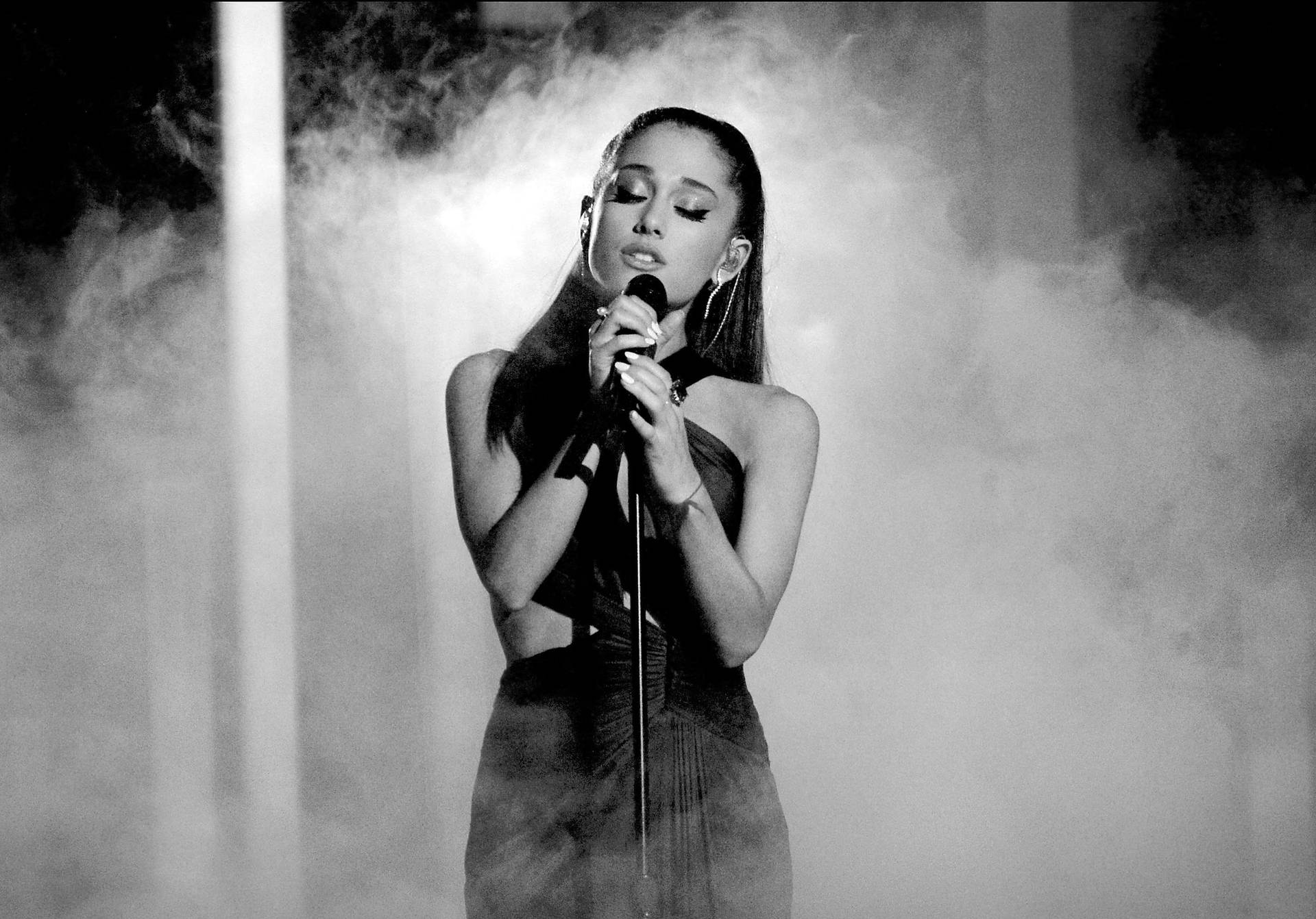歌手Ariana Grande在舞台上表演，伴隨著煙霧和戲劇性的燈光。