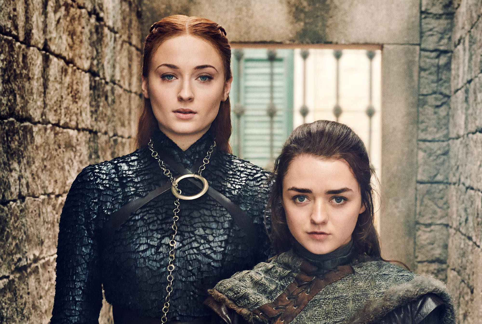 Arya與Sansa Stark，Winterfell姐妹 壁紙 — 兩名身穿中世紀盔甲的兇猛女性莊嚴地站在一面風化的石牆前，身後有一扇帶欄杆的窗戶。