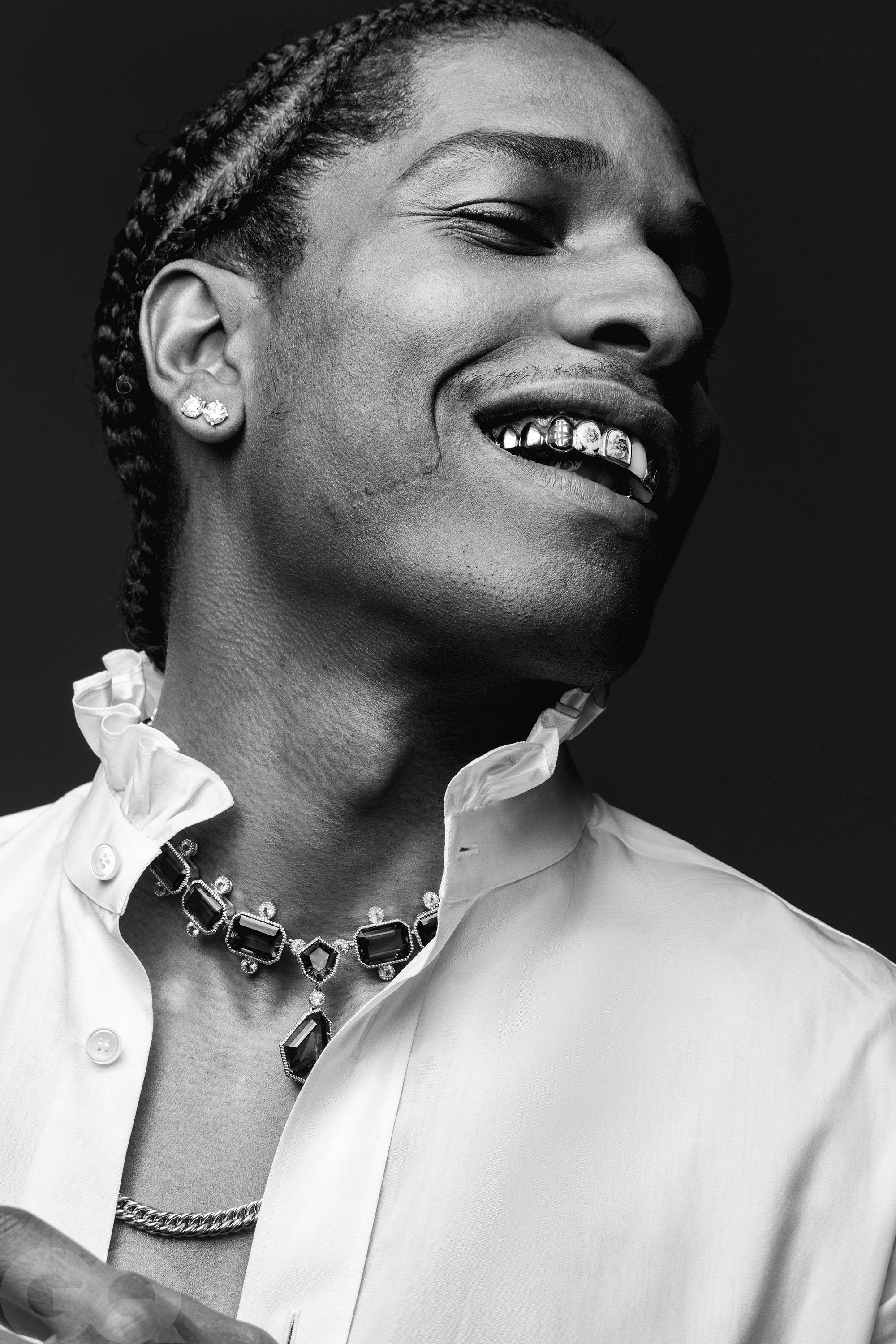 Asap Rocky迷人微笑 壁紙 — 一個微笑的男人黑白肖像，頭髮編成辮子，戴著鑽石牙套，身穿白色襯衫和珠寶項鍊。