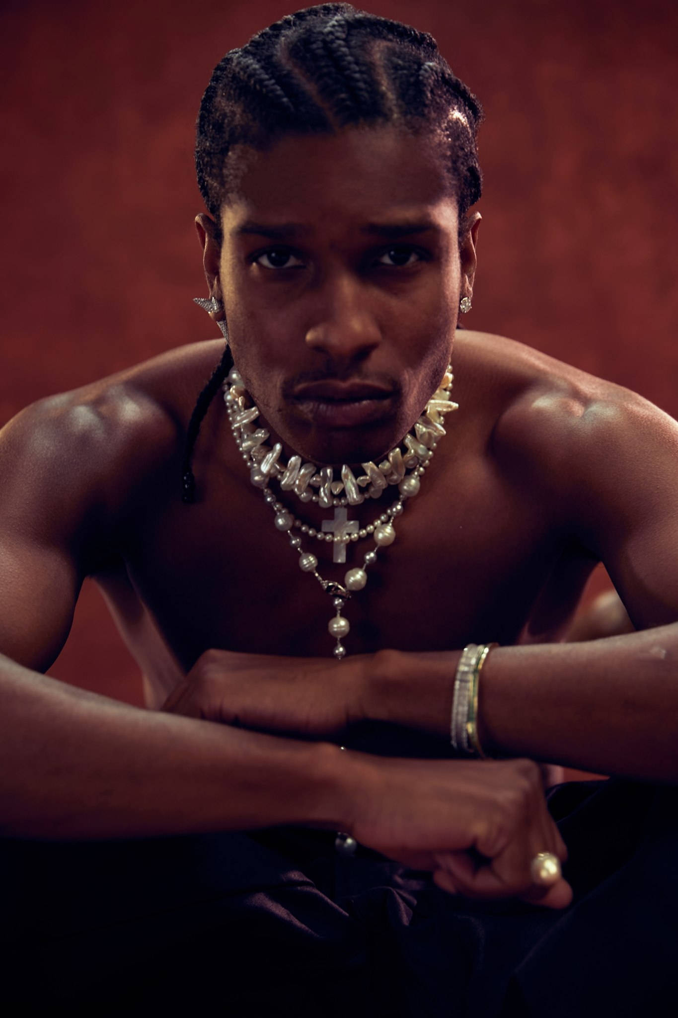帥氣 Asap Rocky 壁紙 — 一個肌肉發達、頭髮編成辮子的男人，在深紅色背景下佩戴著多層珍珠和十字架項鍊，眼神銳利。