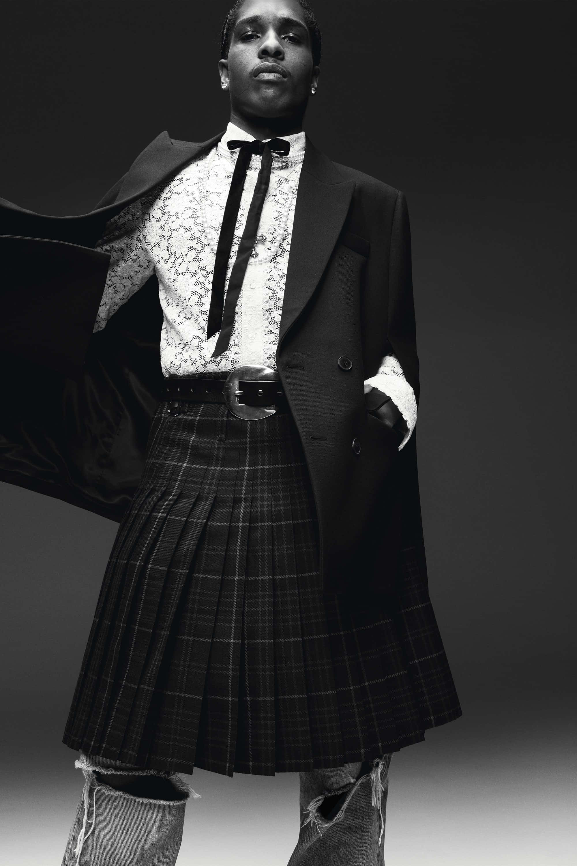 Asap Rocky 與 Tyler 展現個人風格 壁紙 — 一位時尚男士身穿黑色西裝外套和格子裙，在深色工作室背景下自信地擺姿勢。