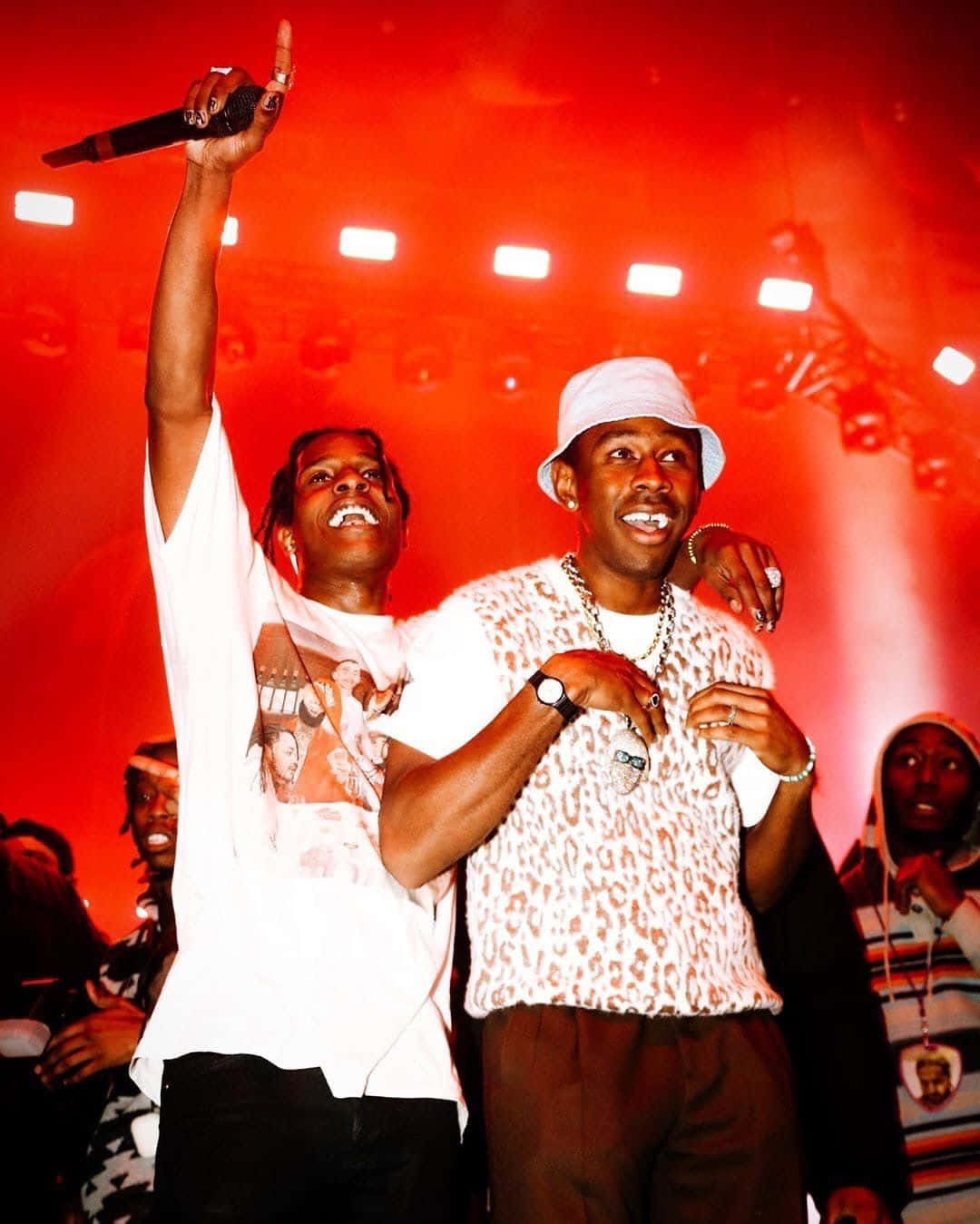 ASAP Rocky 與 Tyler 並肩而立 壁紙 — 兩位饒舌歌手在紅光照耀的舞台上慶祝，一人高舉麥克風，兩人都笑容滿面，充滿活力。
