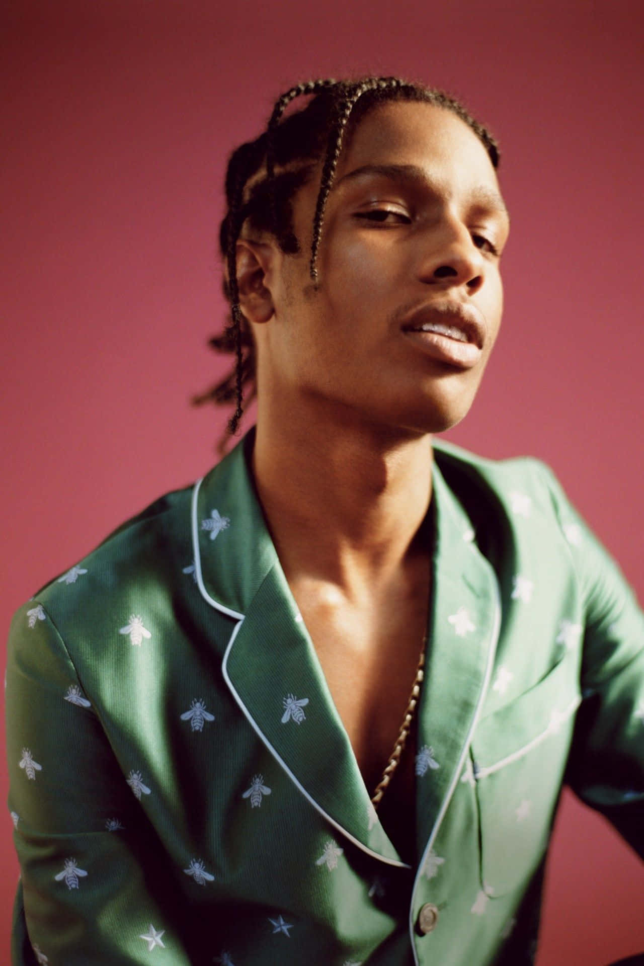 Asap Rocky 以熱情能量引爆現場 壁紙 — 一個辮子頭的人穿著綠色蜜蜂圖案睡衣，背景為純粉紅色。