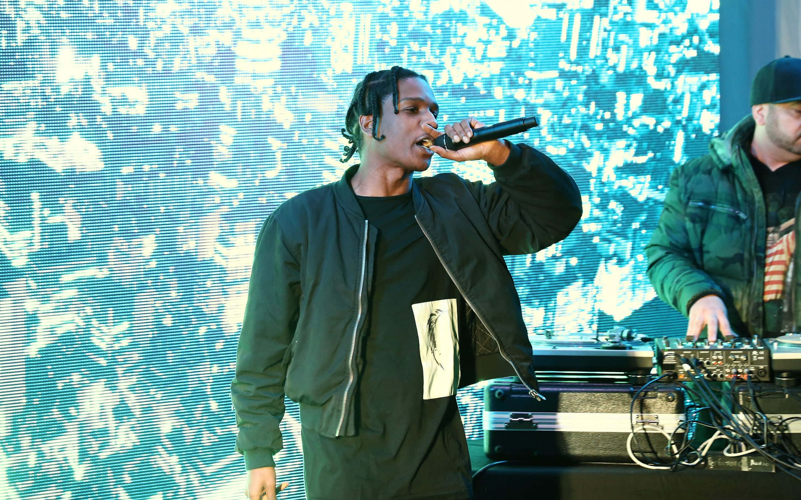 Asap Rocky 即將登台演出 壁紙 — 一位饒舌歌手在舞台上熱情表演，背後有發光的藍色數位背景，旁邊有一位DJ。