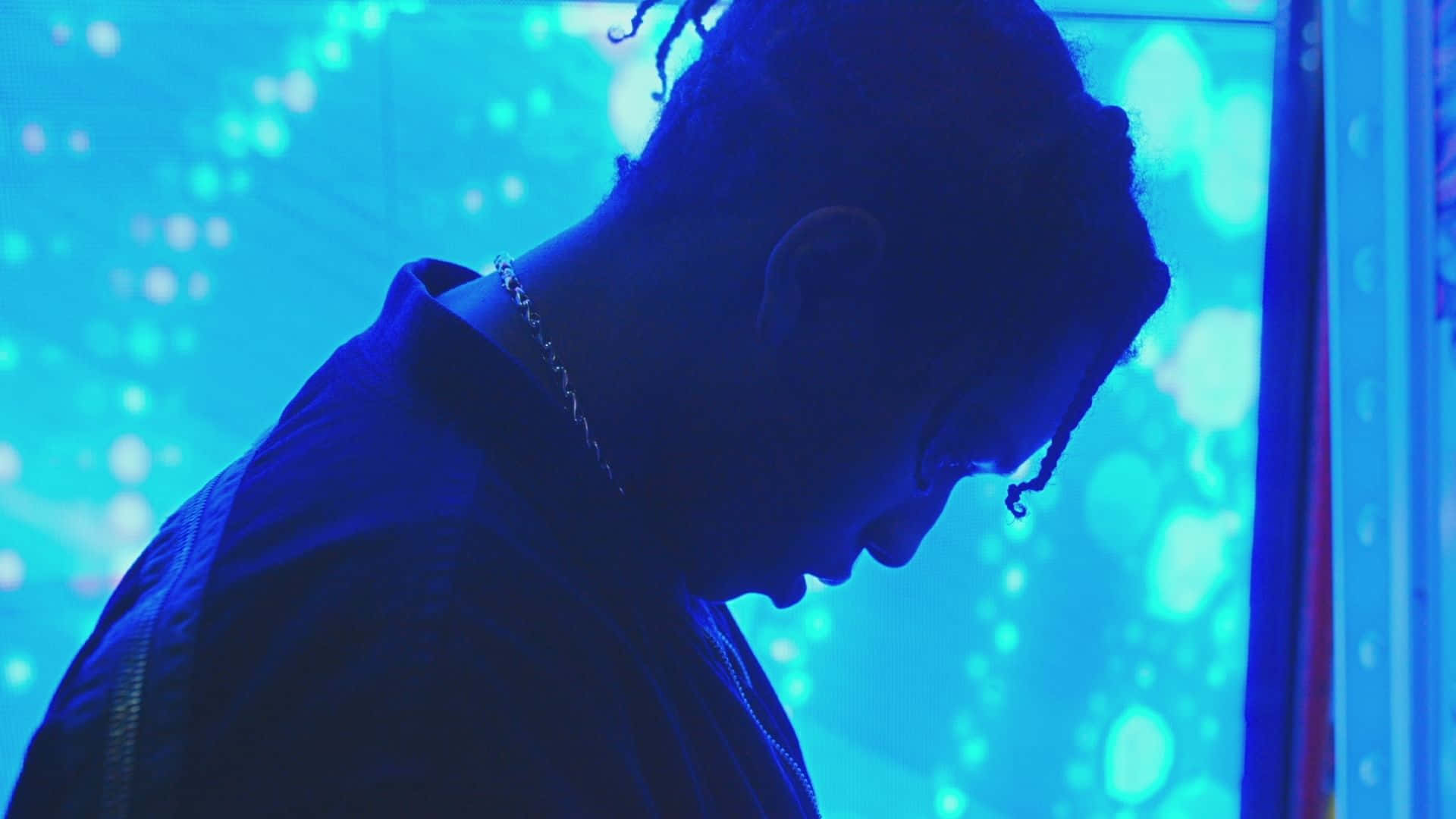 ASAP Rocky 在 The Forum 演唱會現場 壁紙 — 一個留著辮子頭的人以剪影形式出現在發光的藍色數位背景前，帶有散景燈光。