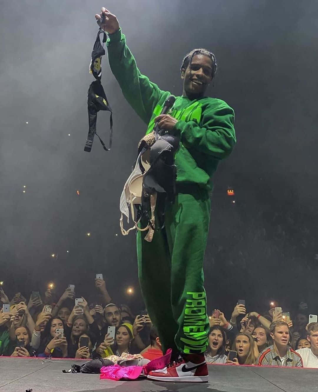 ASAP Rocky與Tyler the Creator，嘻哈傳奇 壁紙 — 一位身穿亮綠色服裝的饒舌歌手在煙霧繚繞的舞台燈光下，愉快地將粉絲禮物拋向歡呼的人群。