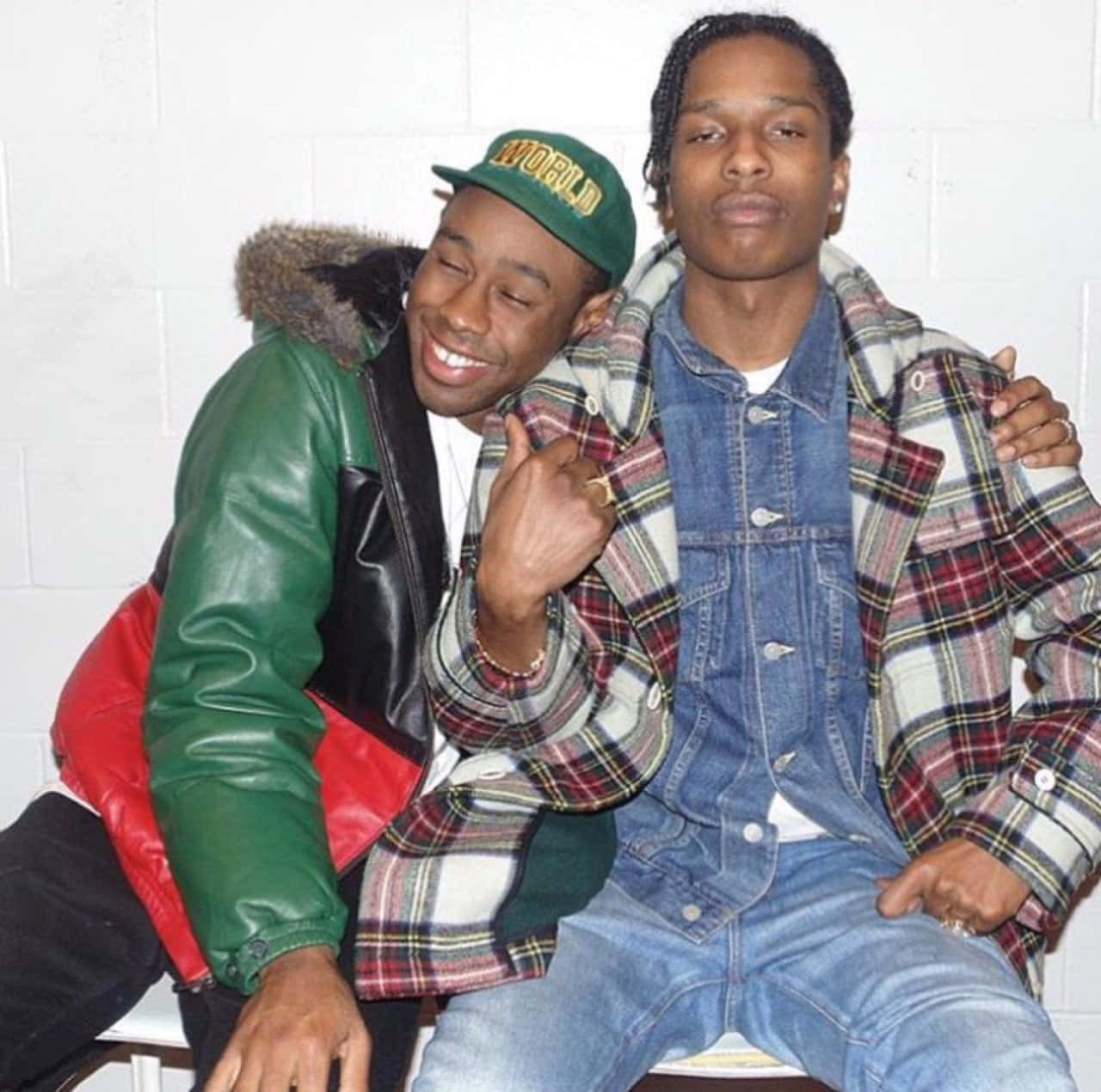 嘻哈音樂合作夥伴ASAP Rocky與Tyler 壁紙 — 兩個男人喺白色磚牆前面隨意擺甫士，一個著綠色、紅色同黑色外套，另一個著格仔牛仔外套。