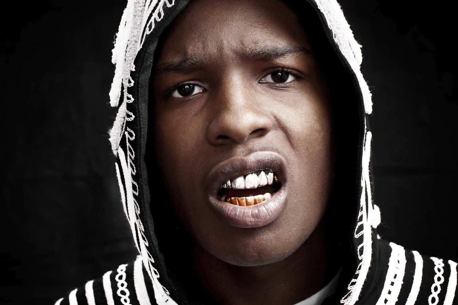 ASAP Rocky出席2017年MTV音樂錄影帶大獎 壁紙 — 一名身穿黑白連帽服裝、戴著金牙的年輕男子在黑暗背景下激烈地露出牙齒。