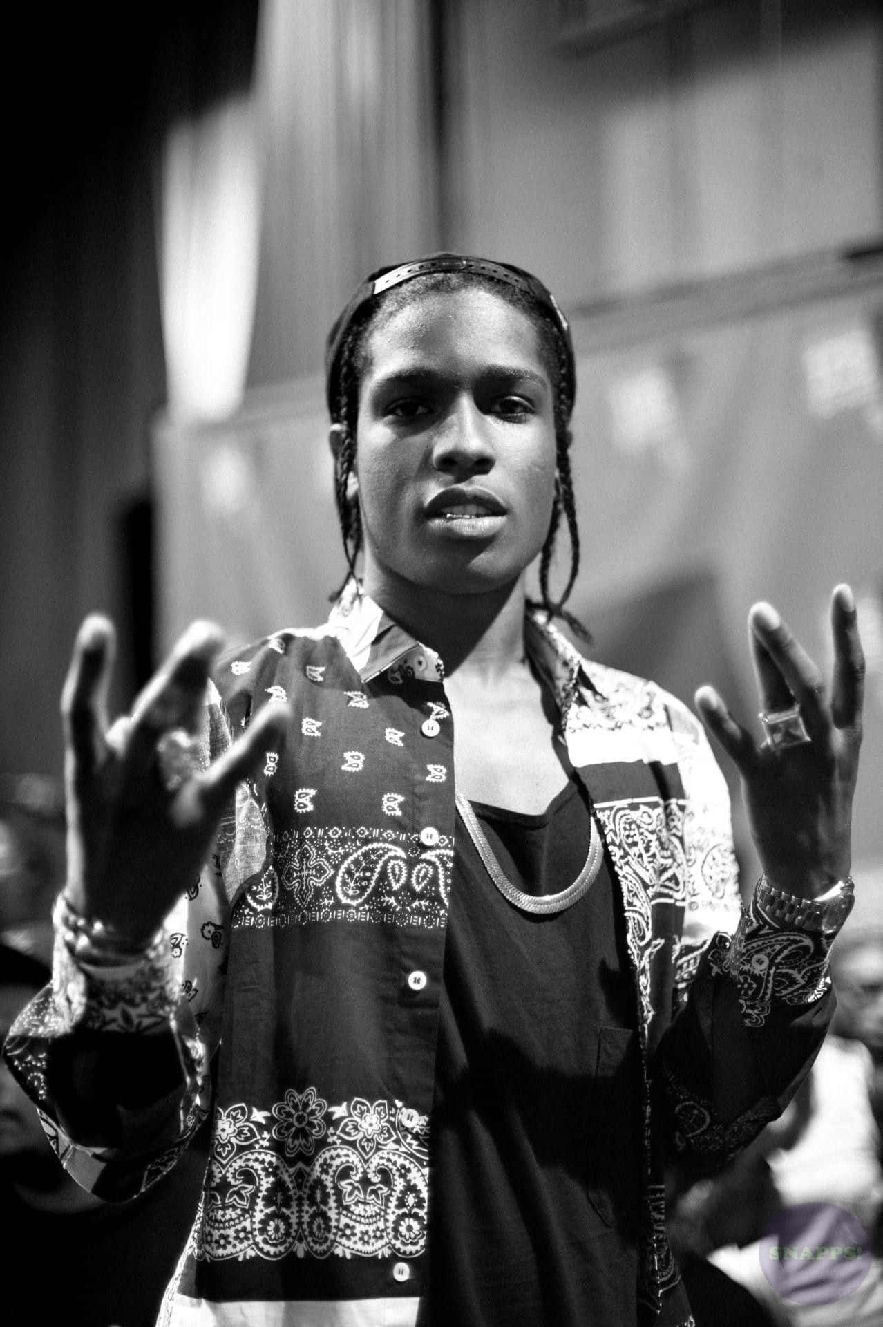 ASAP Rocky宣傳他的最新單曲 壁紙 — 一個年輕男子編著辮子，穿著圖案襯衫，做著手勢的黑白肖像。