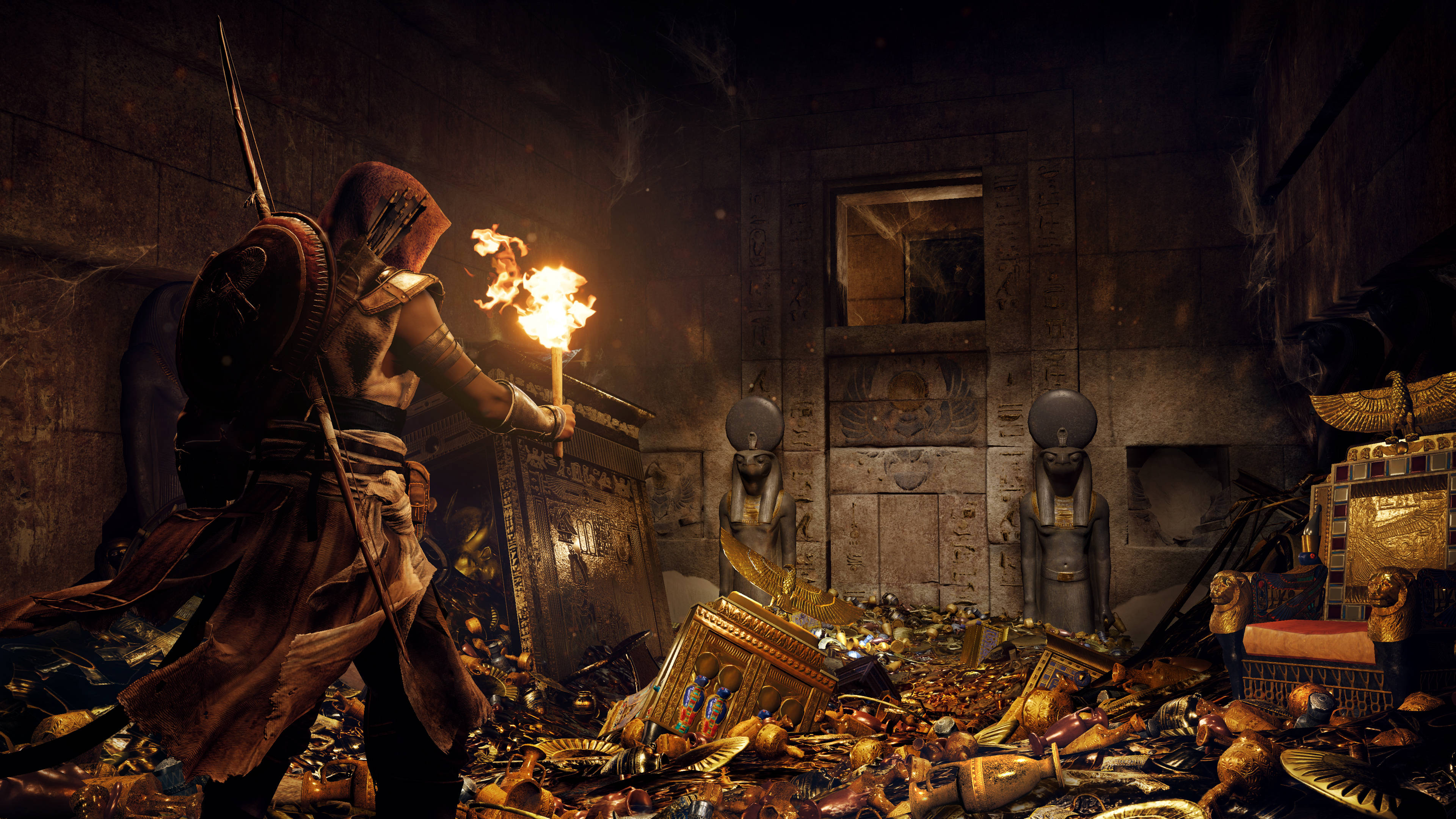 Assassin's Creed Origins 發現寶藏 壁紙 — 一個戴著兜帽的刺客在昏暗的埃及墓穴中手持燃燒的火把，墓穴裡散落著黃金寶藏和石像。