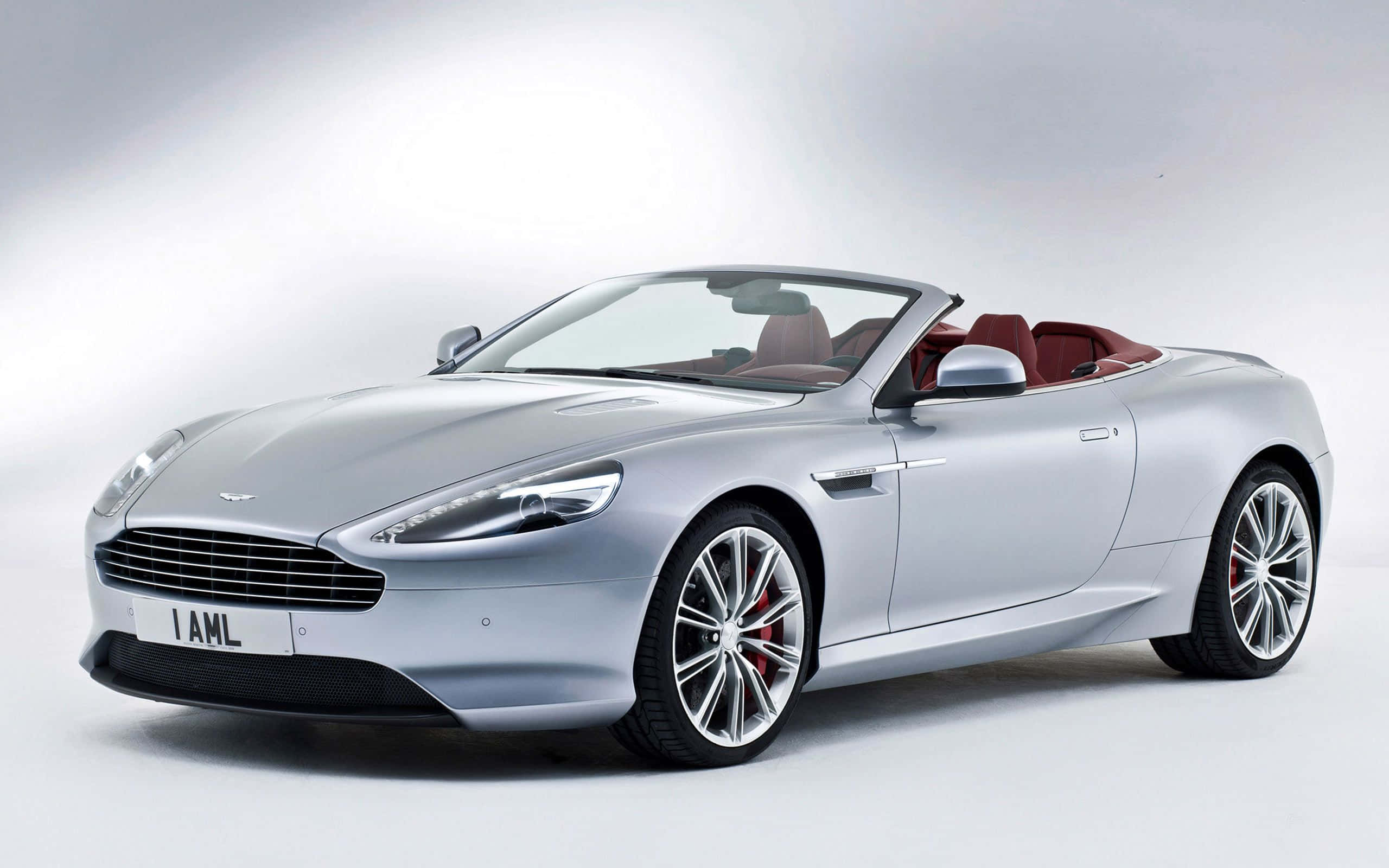 Aston Martin DB9 魅力寫真 壁紙 — 一輛時尚的銀色Aston Martin DB9開篷車，配備紅色內飾和鍍鉻輪圈，在明亮的白色工作室背景前擺拍。