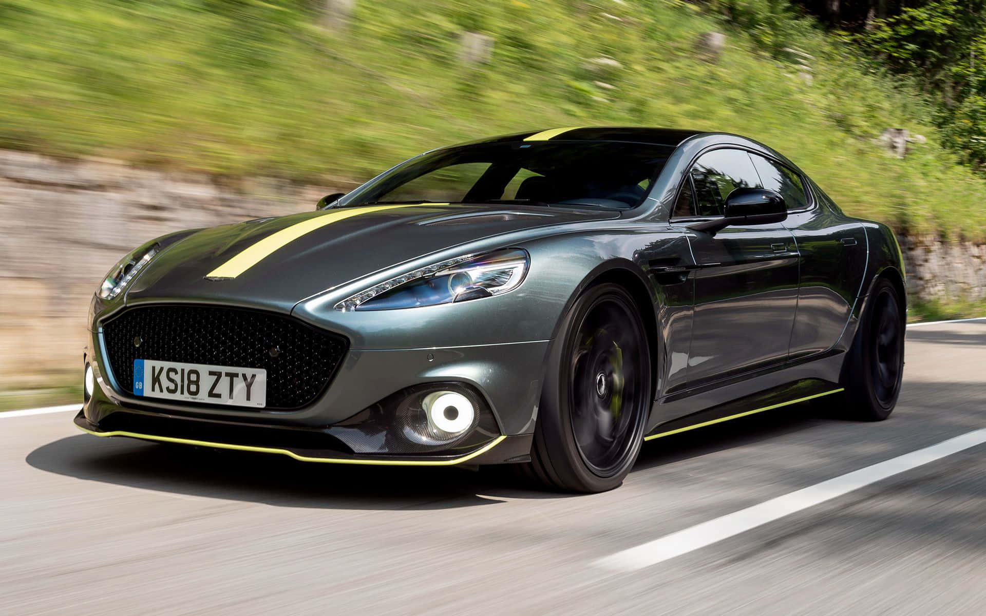 標題：Aston Martin Rapide S – 力量與豪華嘅融合 壁紙 — 一輛帶有黃色點綴的時尚灰色阿斯頓馬丁在蜿蜒的道路上穿過鬱鬱蔥蔥的綠色山丘飛馳。