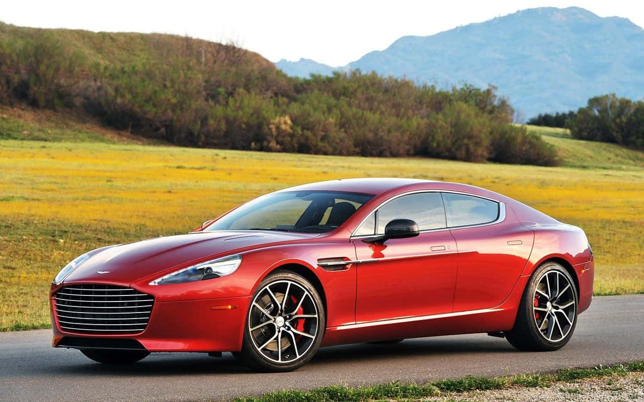 Aston Martin Rapide S：時尚奢華與性能 壁紙 — 一架流線型紅色Aston Martin跑車沿著蜿蜒的道路行駛，穿過陽光明媚的田野，遠山在望。