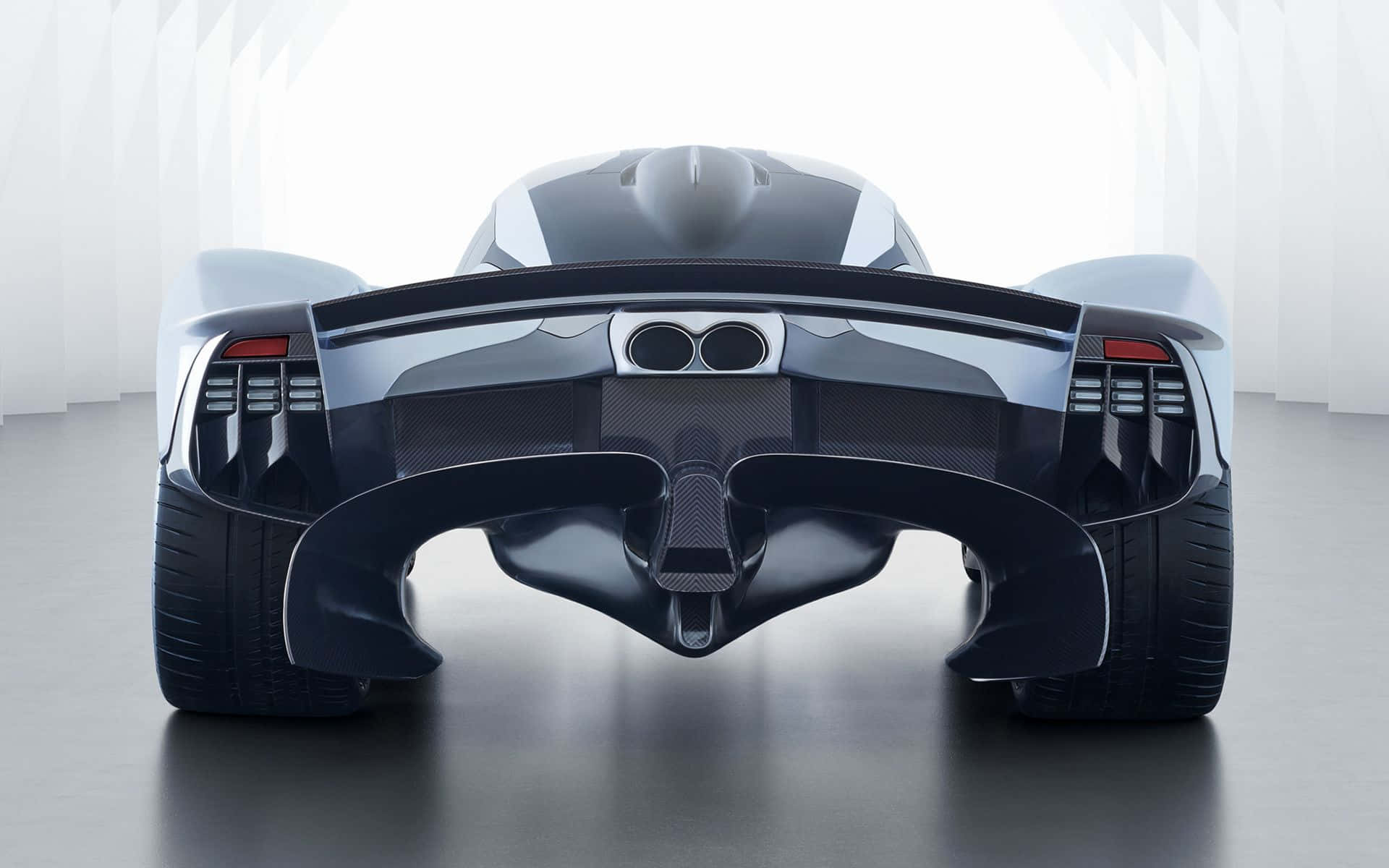 Aston Martin Valkyrie - 夢幻機器行動中 壁紙 — 在一個簡約的工作室中，從後方觀看一輛時尚的未來主義跑車，工作室有明亮的白色牆壁和反光地板。