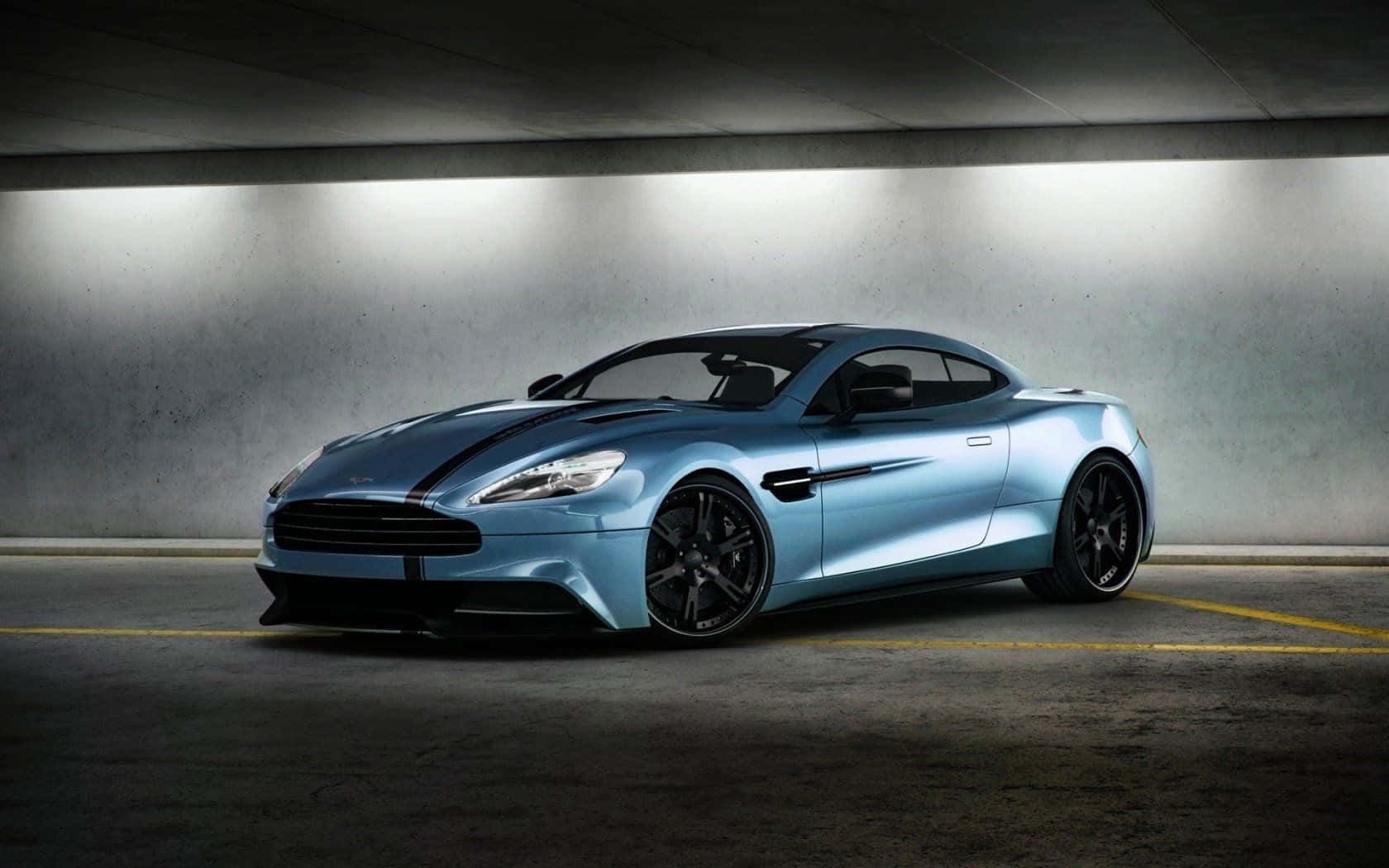 流暢奔馳嘅Aston Martin Vanquish 壁紙 — 一輛時尚的淺藍色 Aston Martin 跑車帶有黑色條紋，在混凝土地下停車場的明亮燈光下閃閃發光。