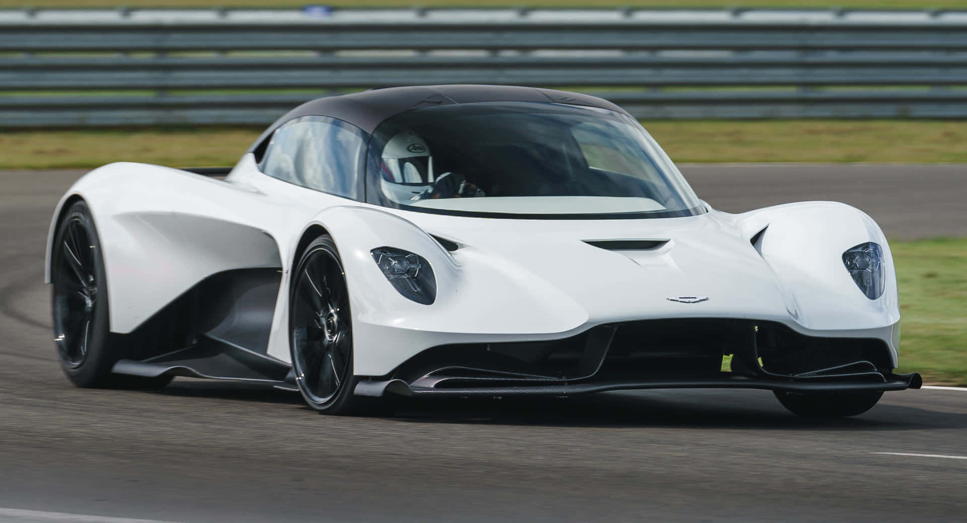 駕駛 Aston Martin，踏上冒險之旅 壁紙 — 一架流線型白色Aston Martin Valkyrie賽車在賽道上疾馳，背景有模糊的動感和綠色草地。