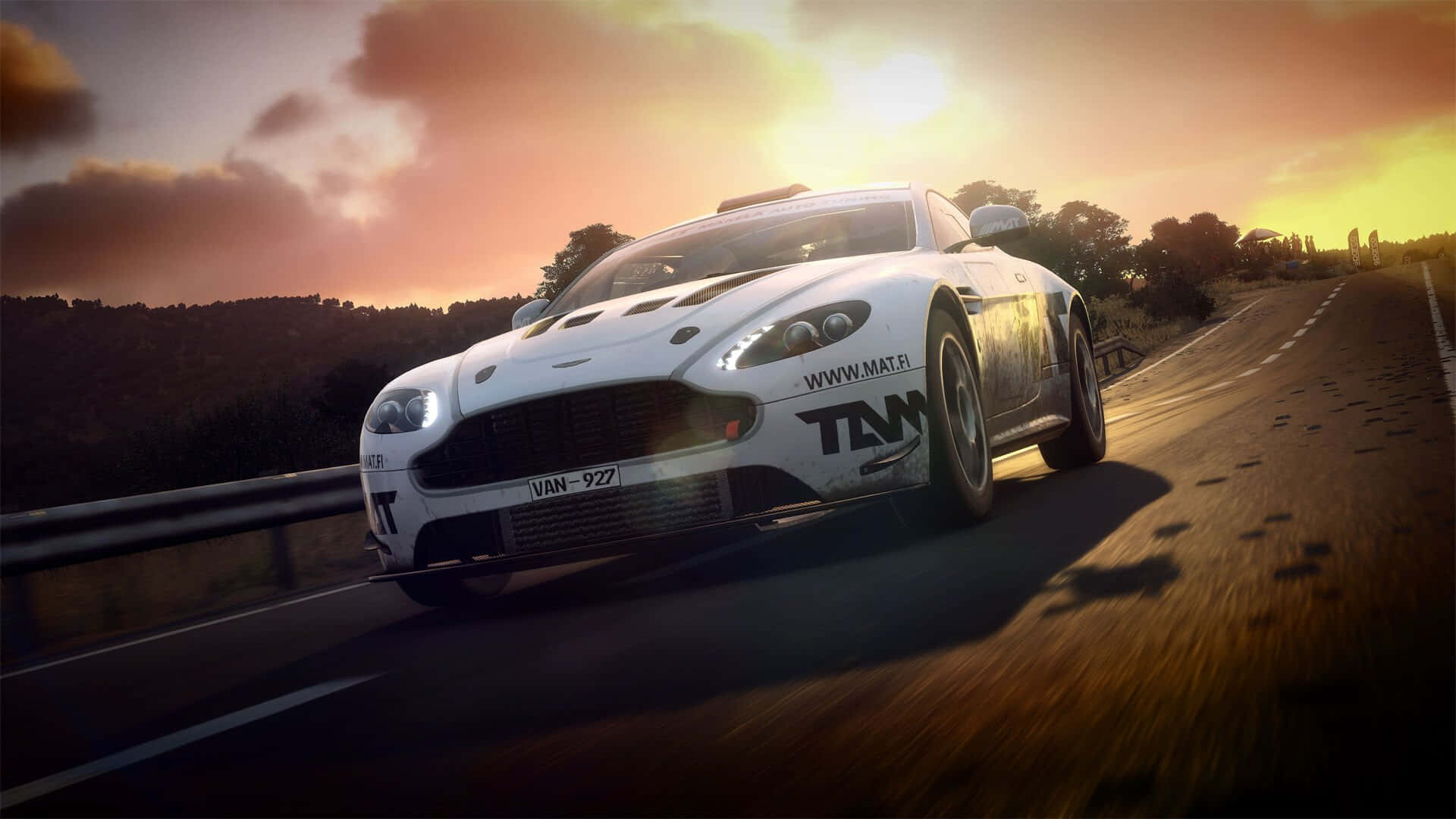 Aston Martin最佳越野拉力賽背景 壁紙 — 一輛白色Aston Martin賽車在日落時分沿著蜿蜒的道路疾馳，伴隨著溫暖的金色光芒和戲劇性的雲彩。